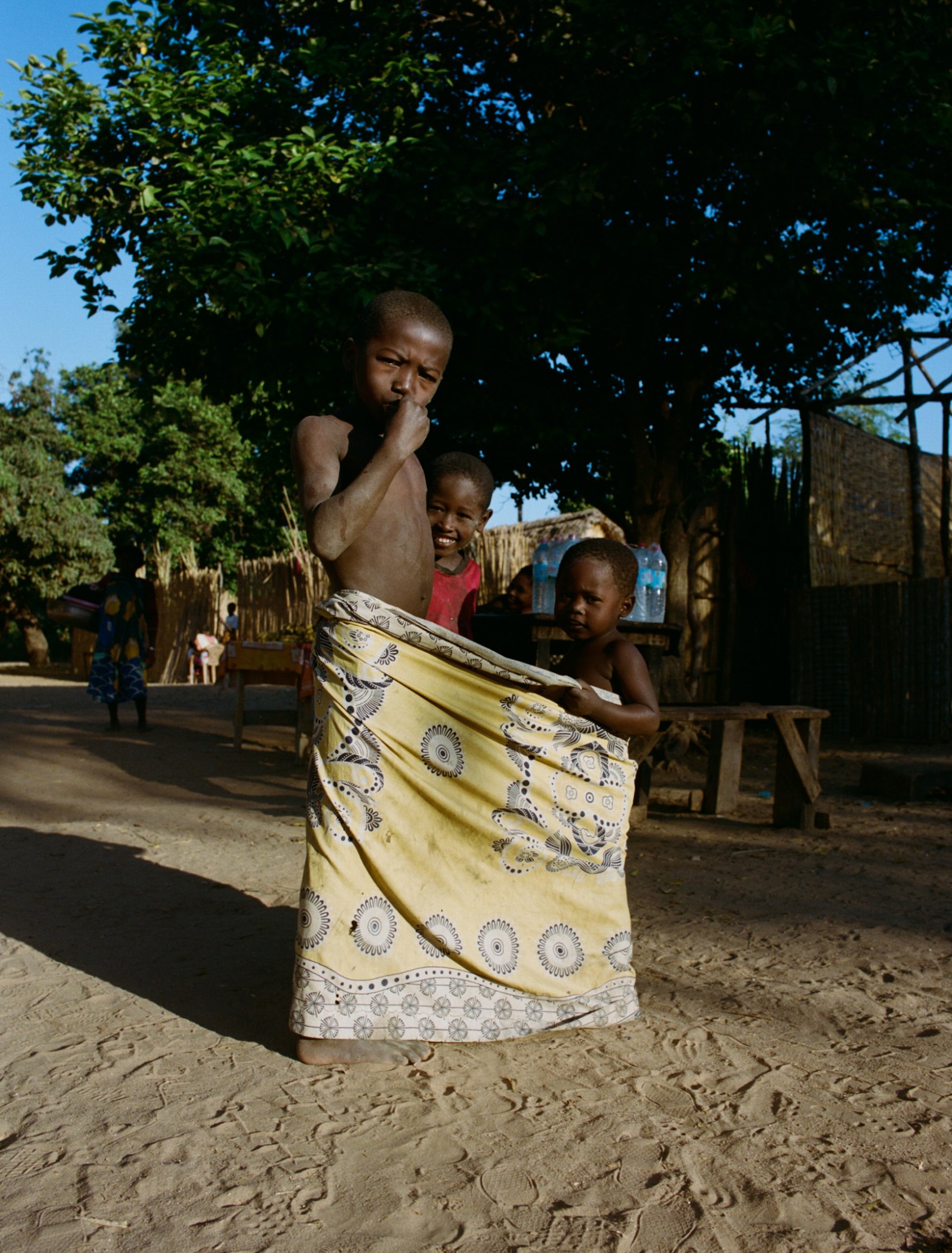 three young children wrapped in a yellow cloth on a sandy street