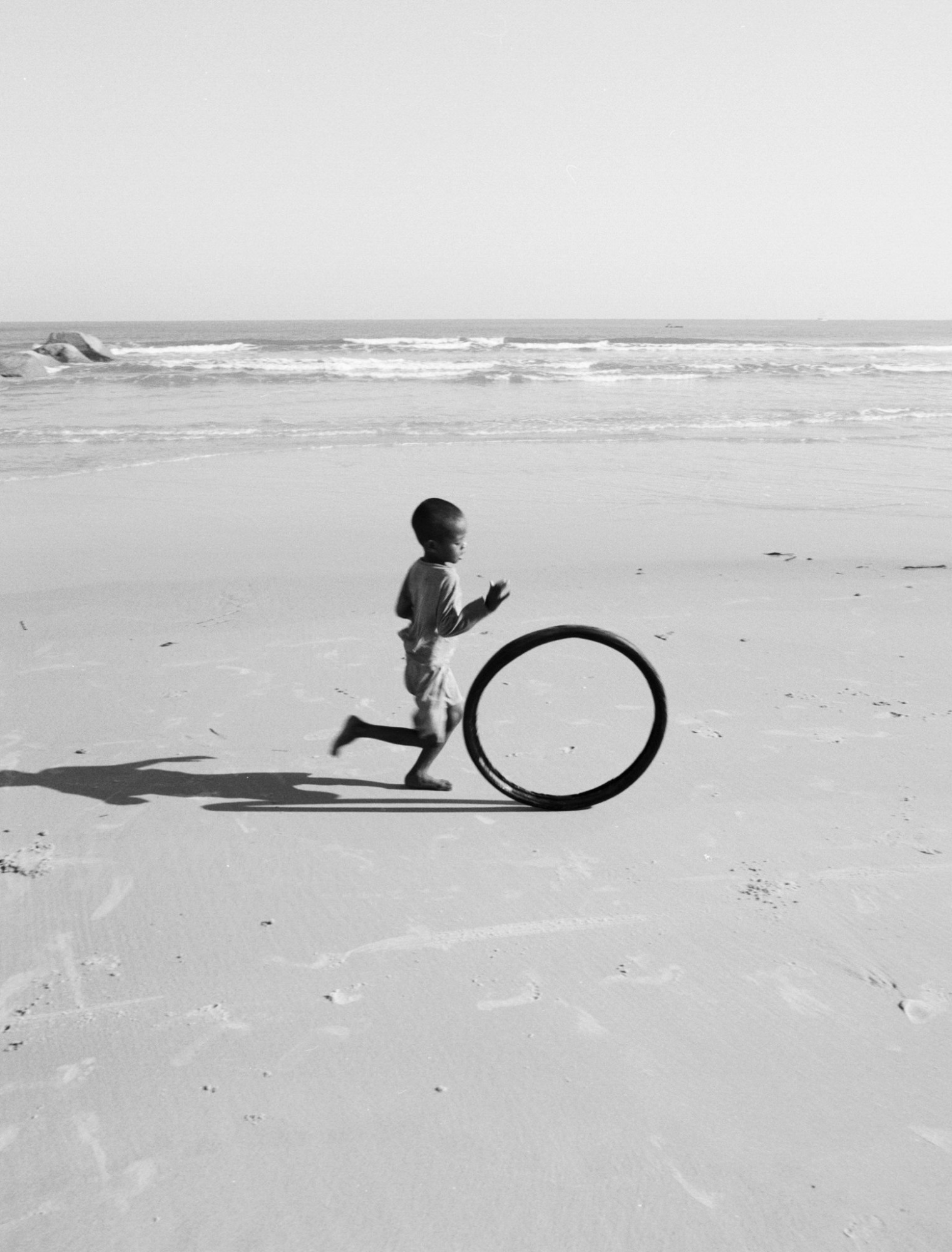 a young boy chasing a bicycle tire on the beach