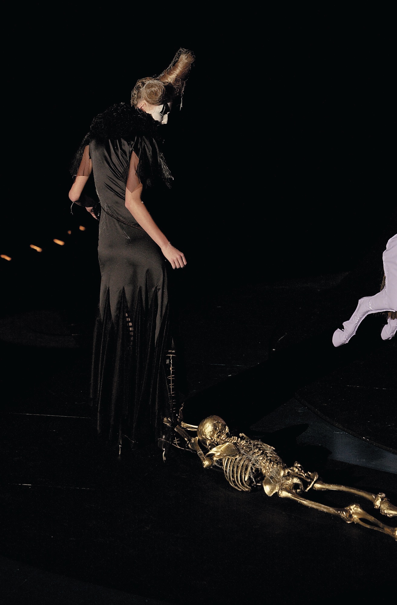 A model walking for Alexander McQueen AW01 with a gold skeleton hanging from her dress.