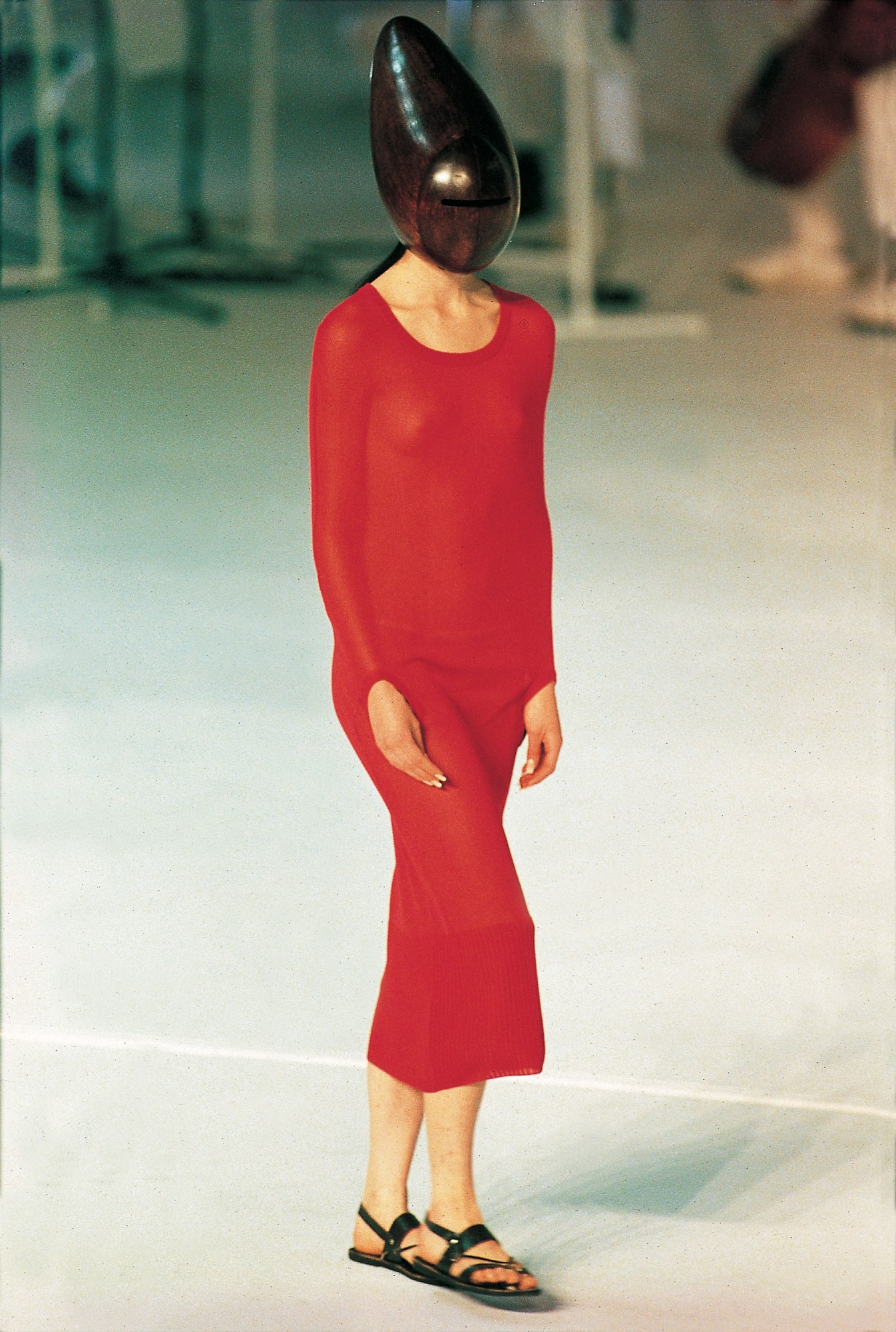 A model walking for Hussein Chalayan SS98 in a red dress and sandals with a helmet