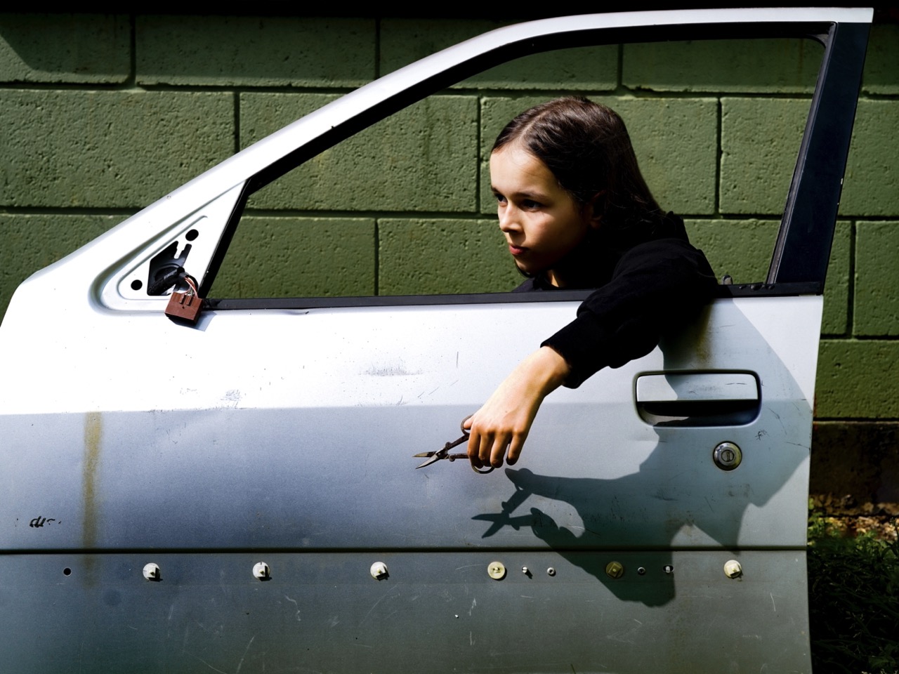 A girl holding scissors sitting behind a car door by Felice Ito for her CSM graduate project