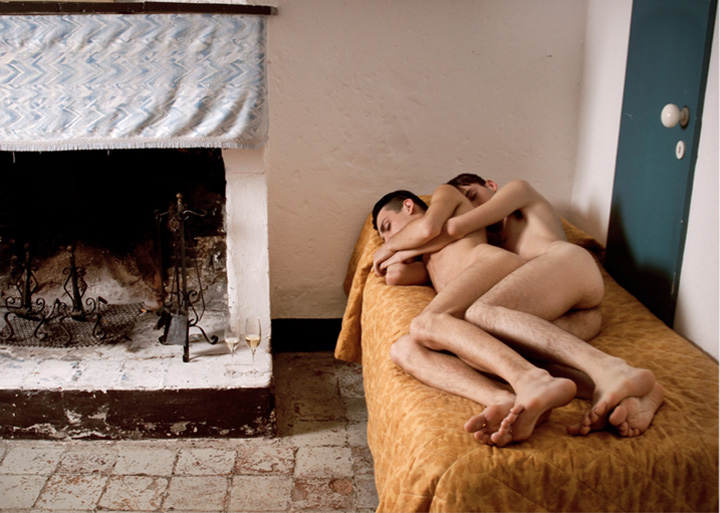 a couple lying in a small bed near a fireplace