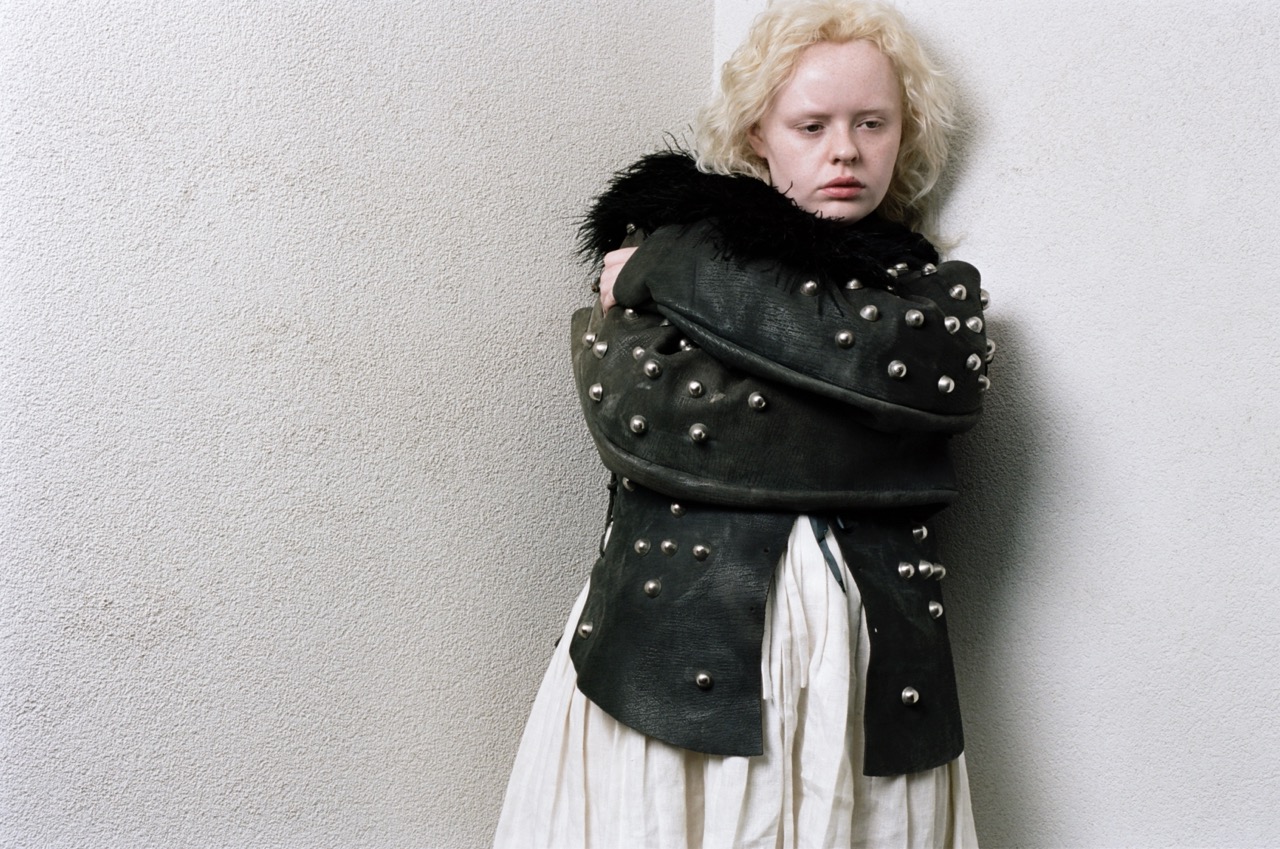 CSM graduate project of Alisa Dyundik of a girl wearing a black jacket covered in balls and a white dress skirt holding herself