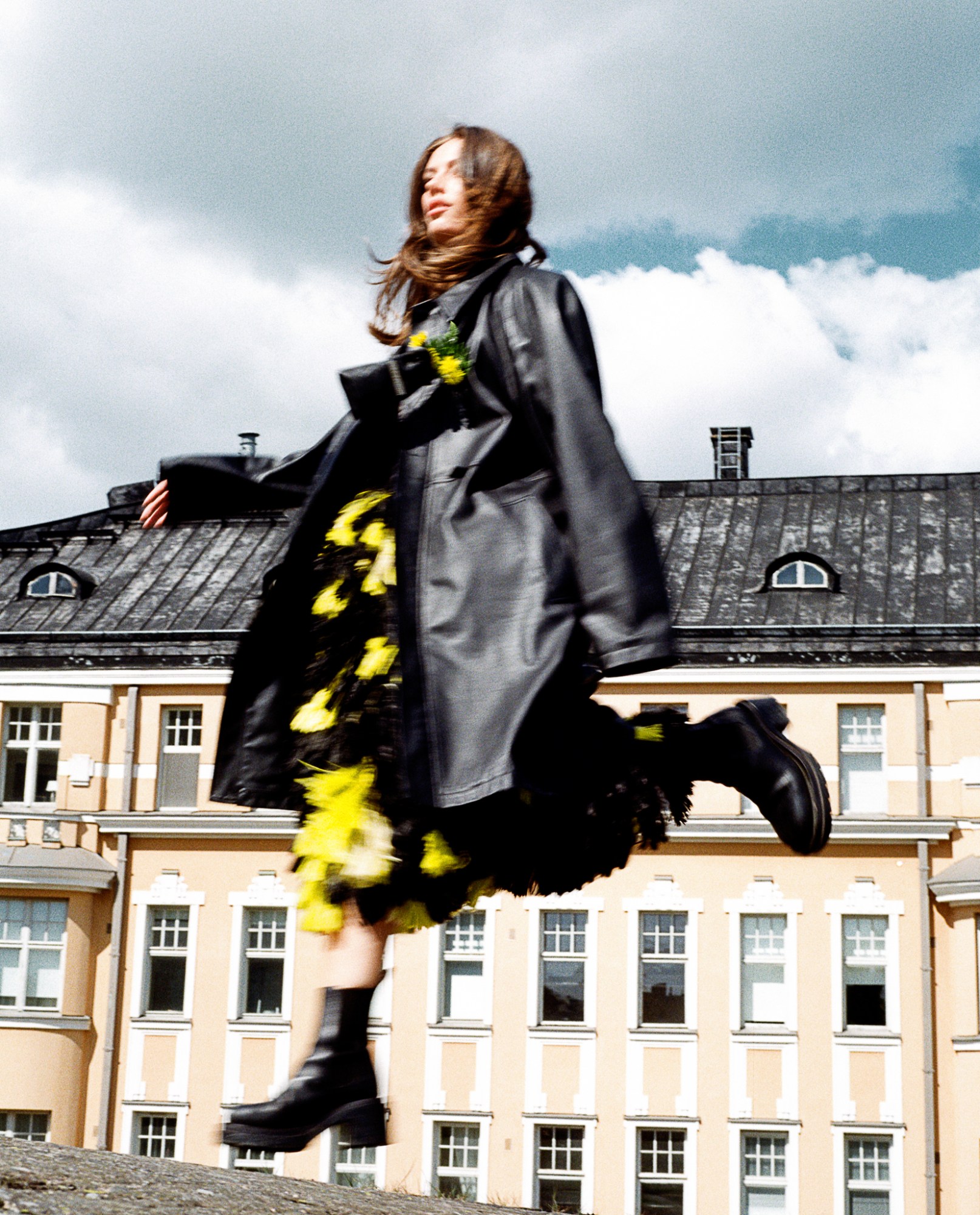 a model jumping in black and yellow pattern dress in a blurry photo by simone steenberg