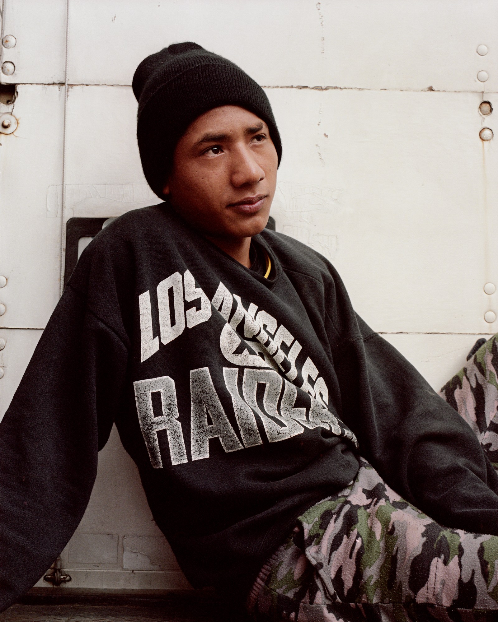 a guatemalan teen lounging in an oakland raiders sweatshirt and black hat