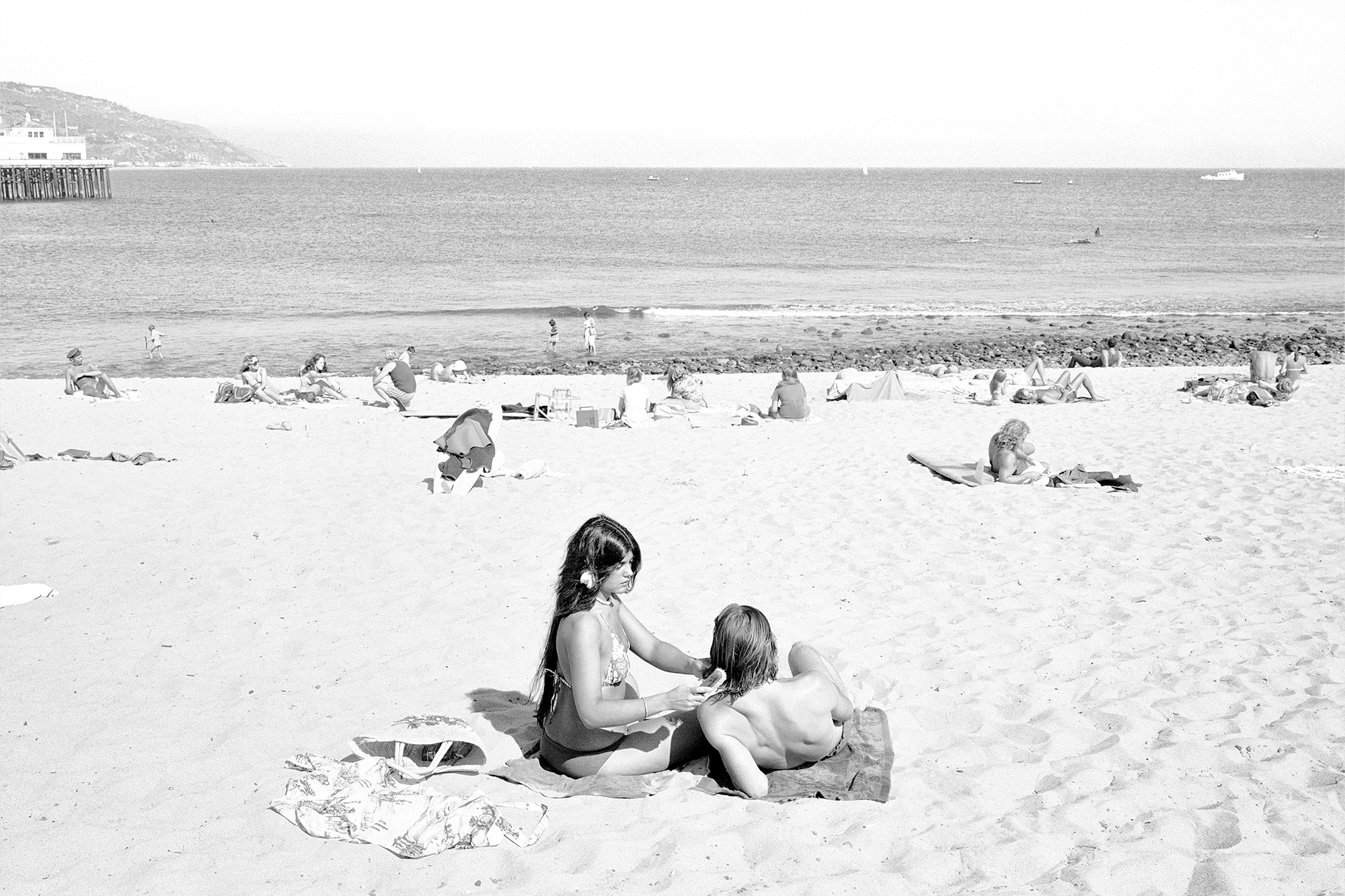 black-and-white image of a couple lounging on towels on a busy beach