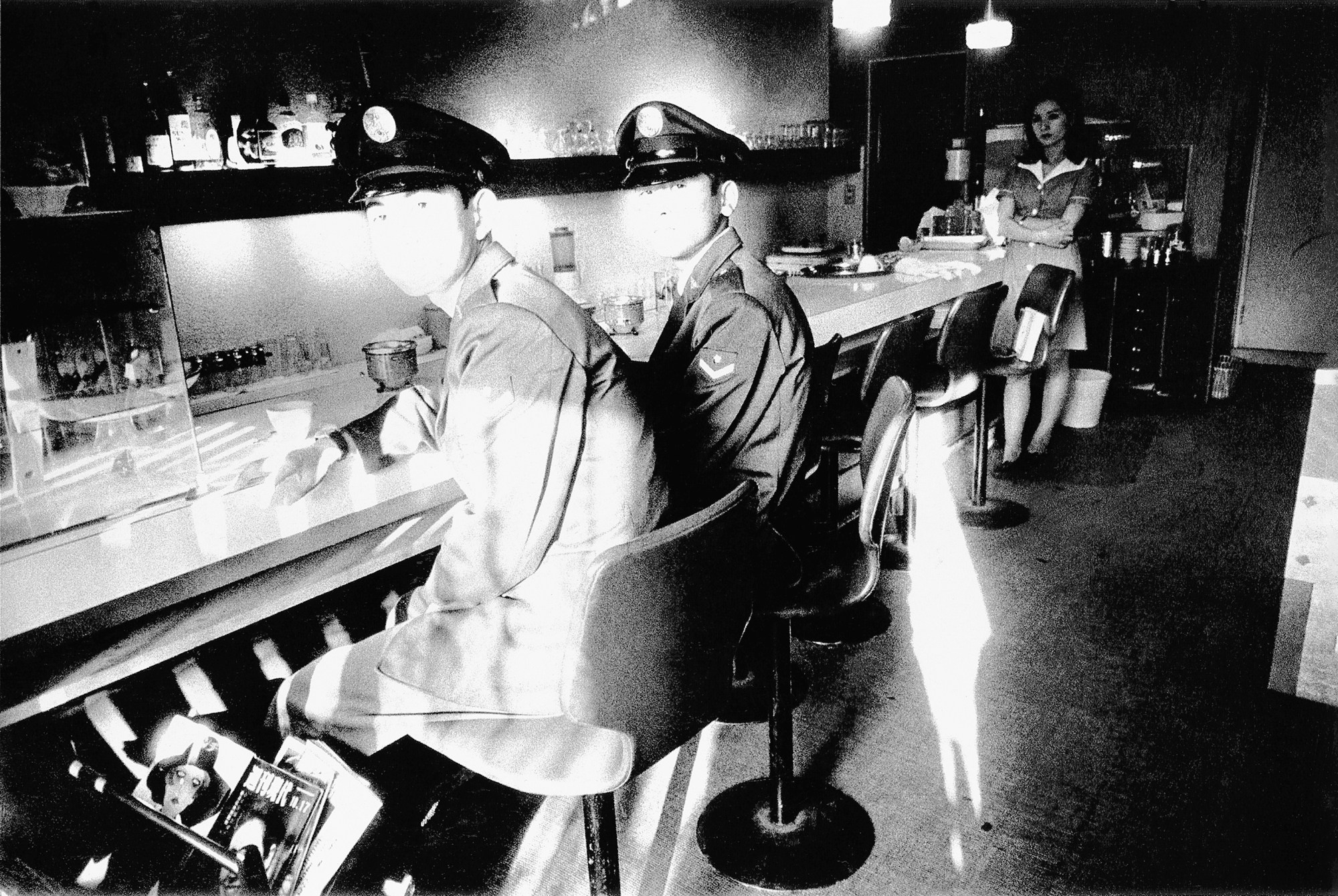 two marines in full uniform sitting at a bar, looking at the camera. a waitress stands behind them.