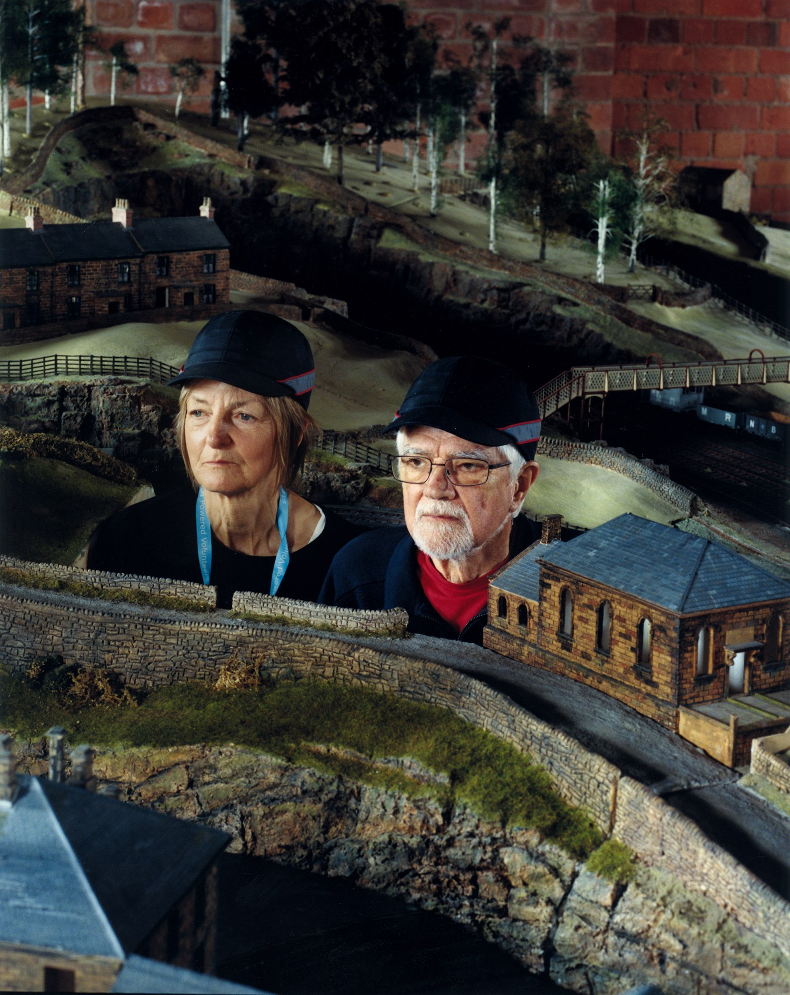 a photograh of two people dressed like train conductor with their heads poking out of a model village