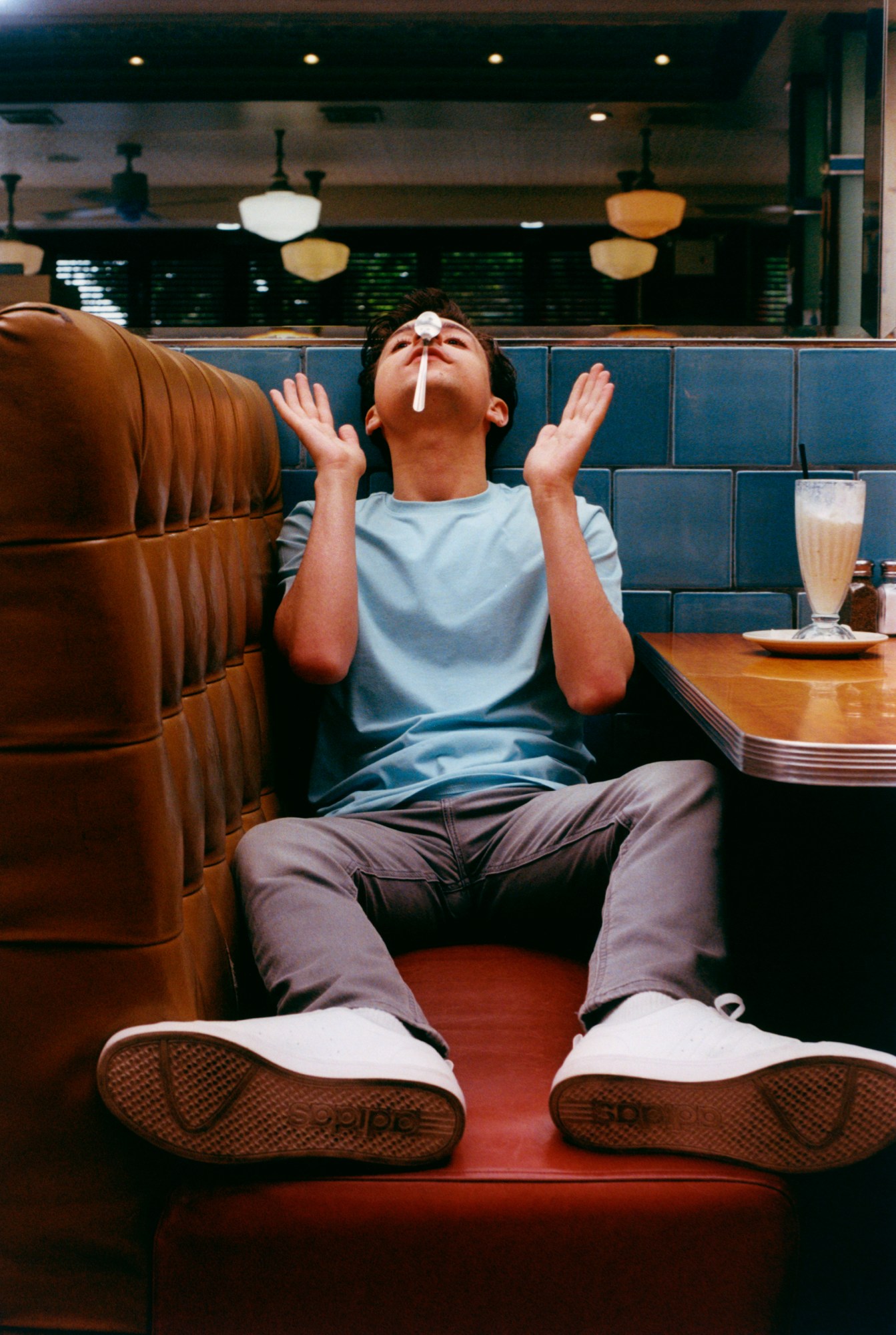 jake ryan actor balances a spoon on his nose on a red sofa in remedy diner new york city