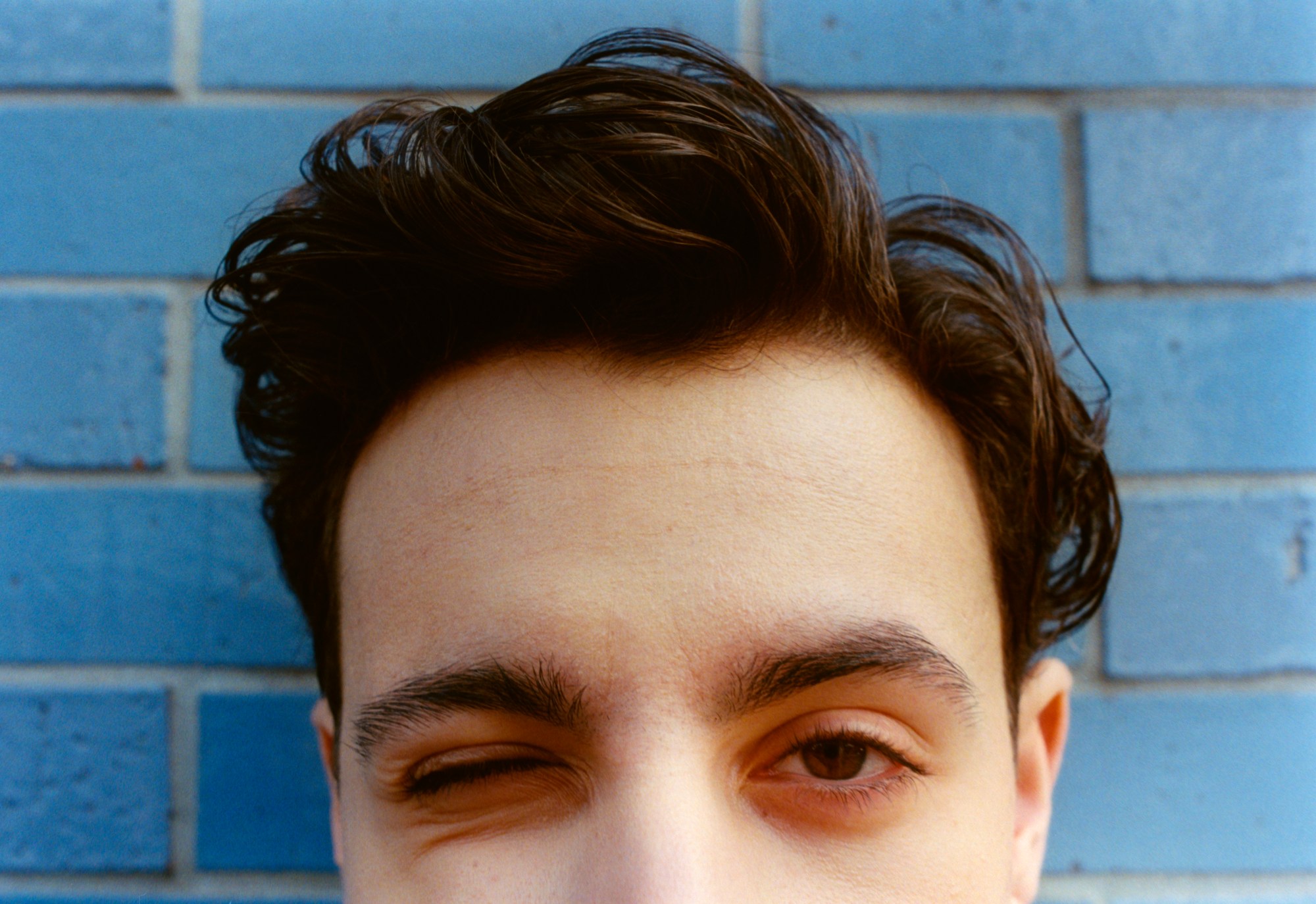 close crop of jake ryan actor winking against a blue brick wall