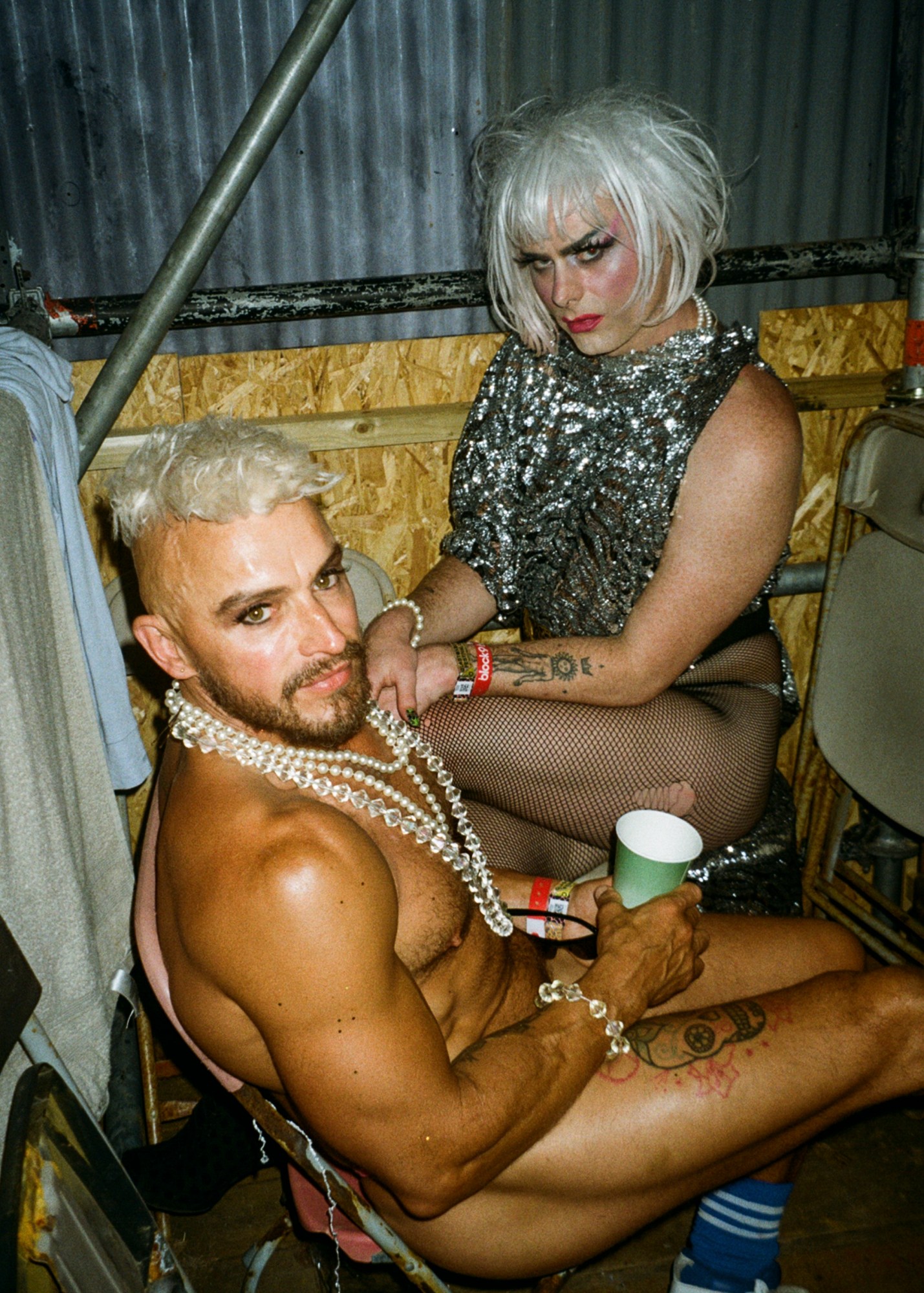 a club goer wearing clear beads sitting next to a friend in a platinum blonde wig