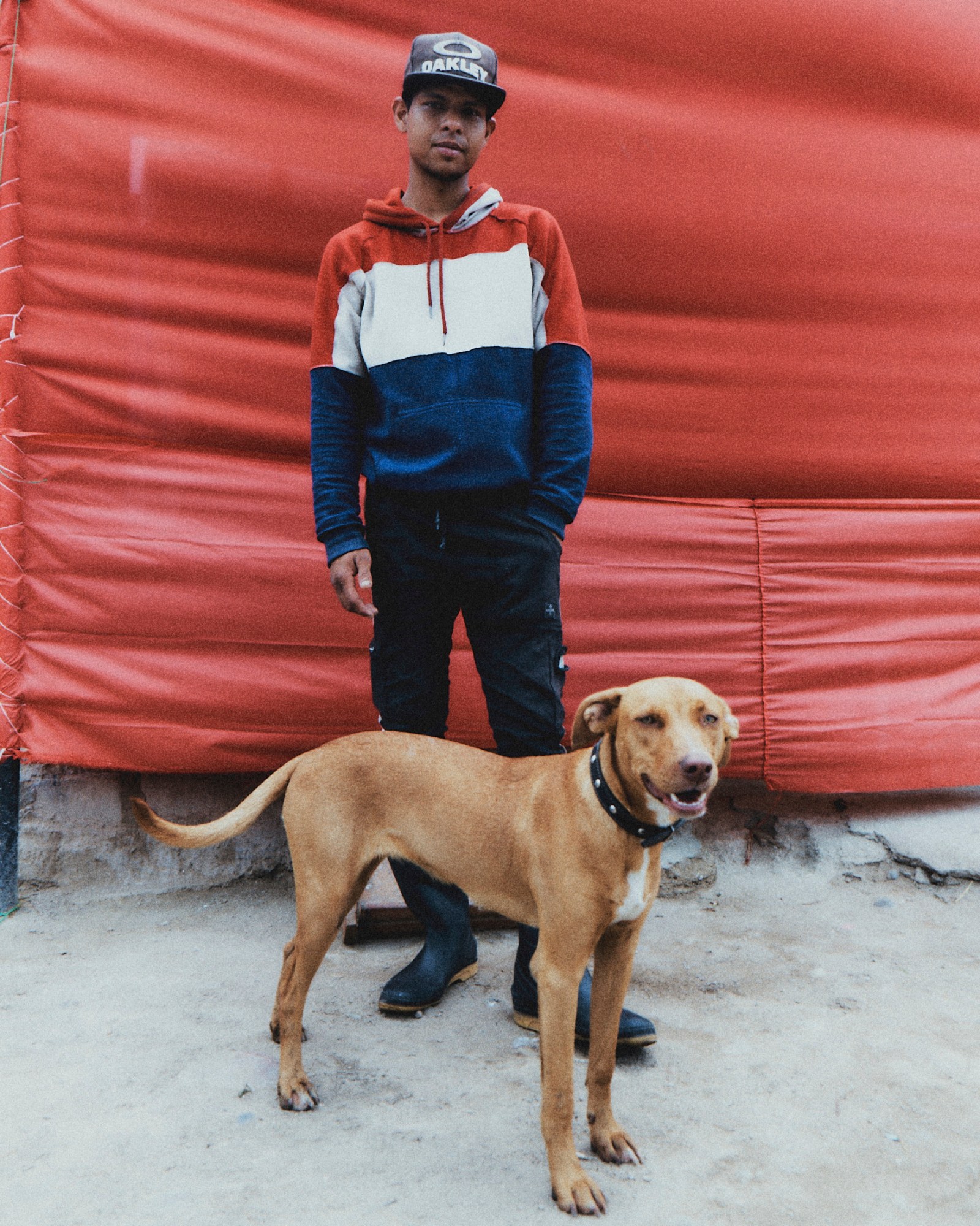 a man in a red white and blue hoodie posing in front of a red flag with his dog in peru