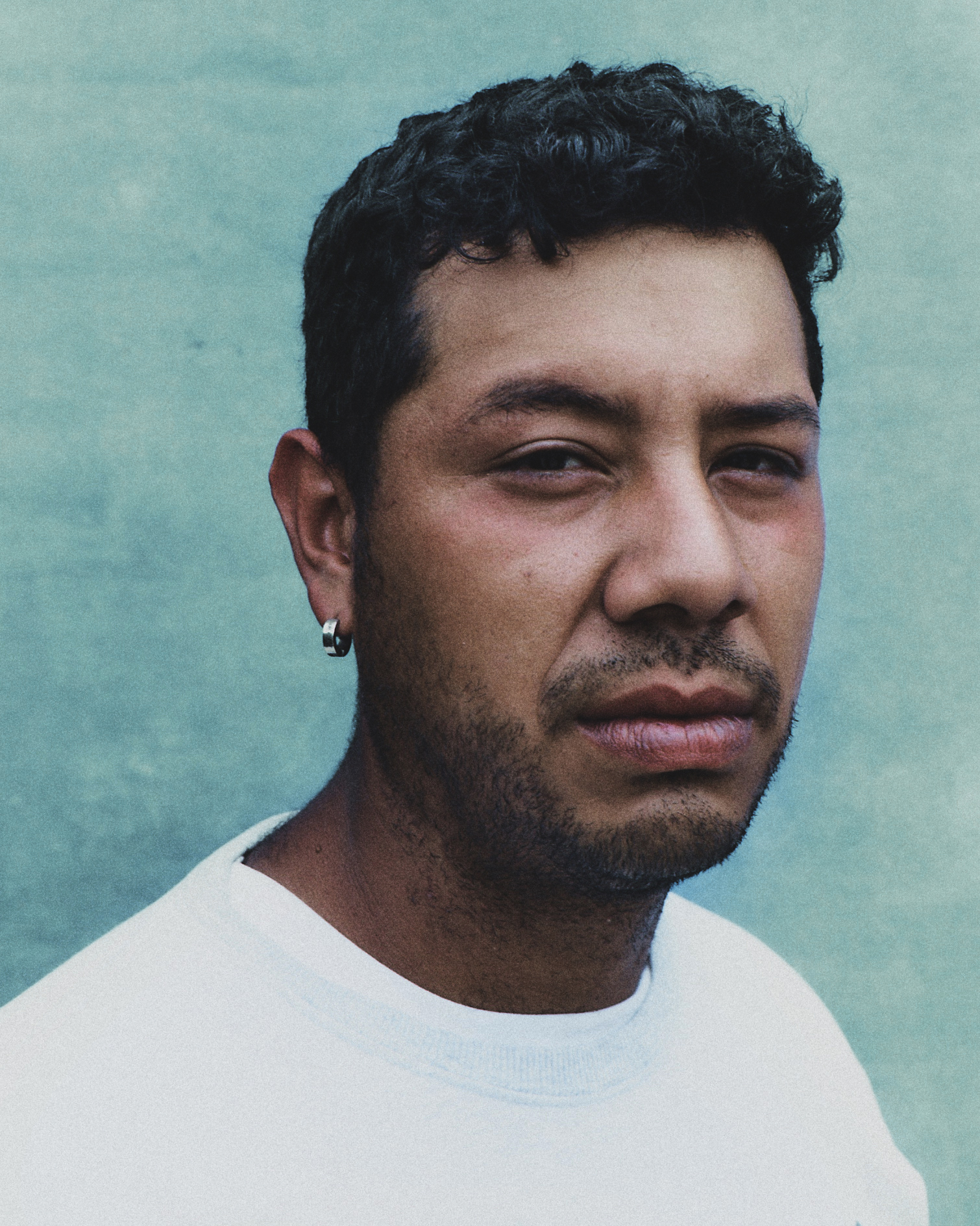 a venezuelan man in a white sweatshirt against a teal wall looking into the camera