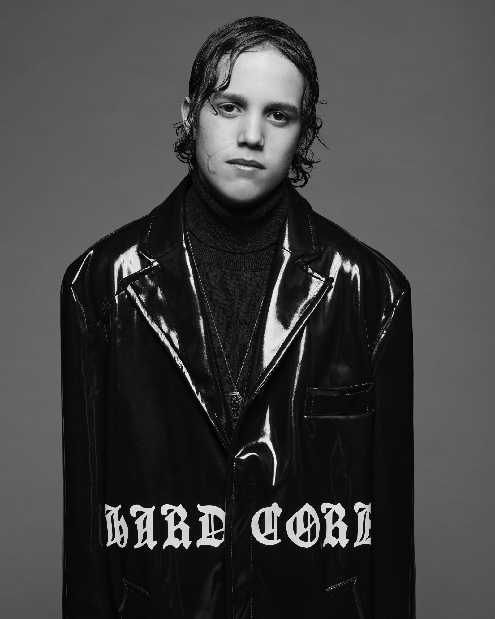 a kid wearing a long shiny black coat shot in a studio