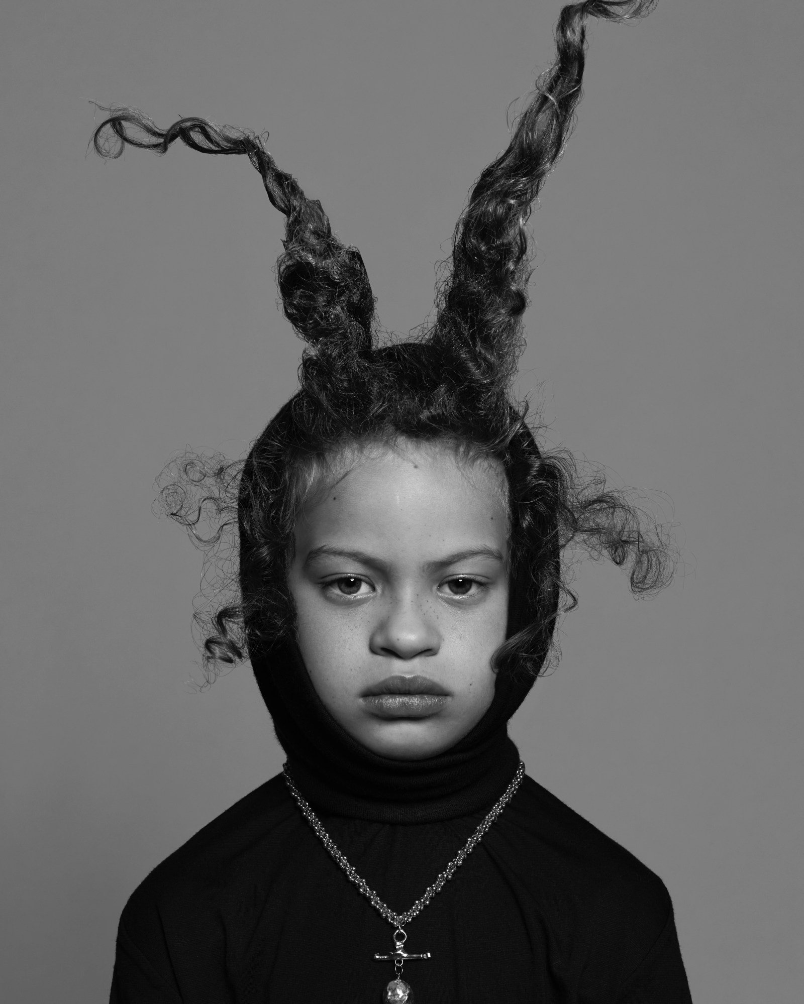 a kid wearing two bits of their hair spiked up and a black hood shot in a studio