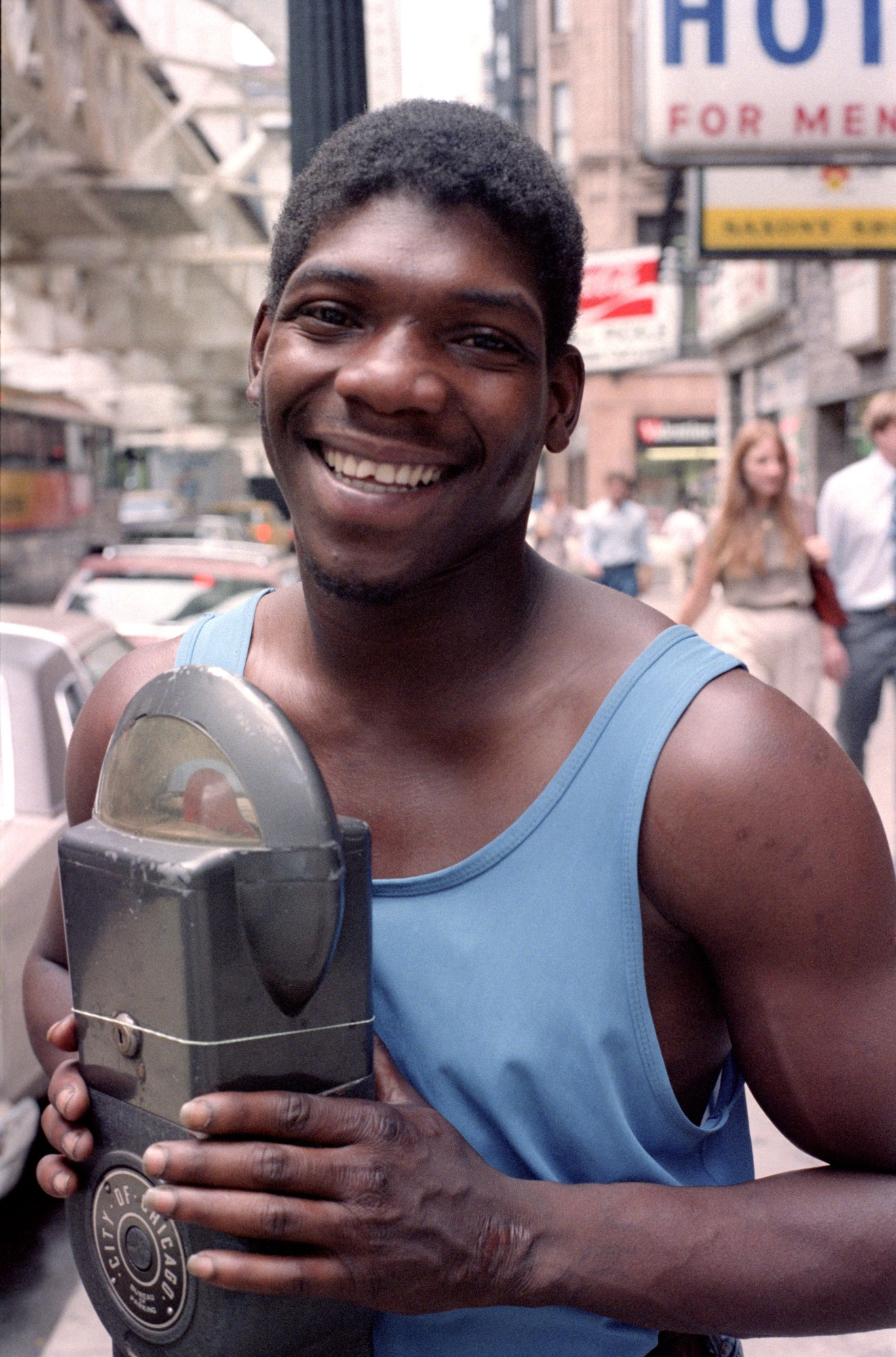 a man in a blue tank top posing next to a parking meter