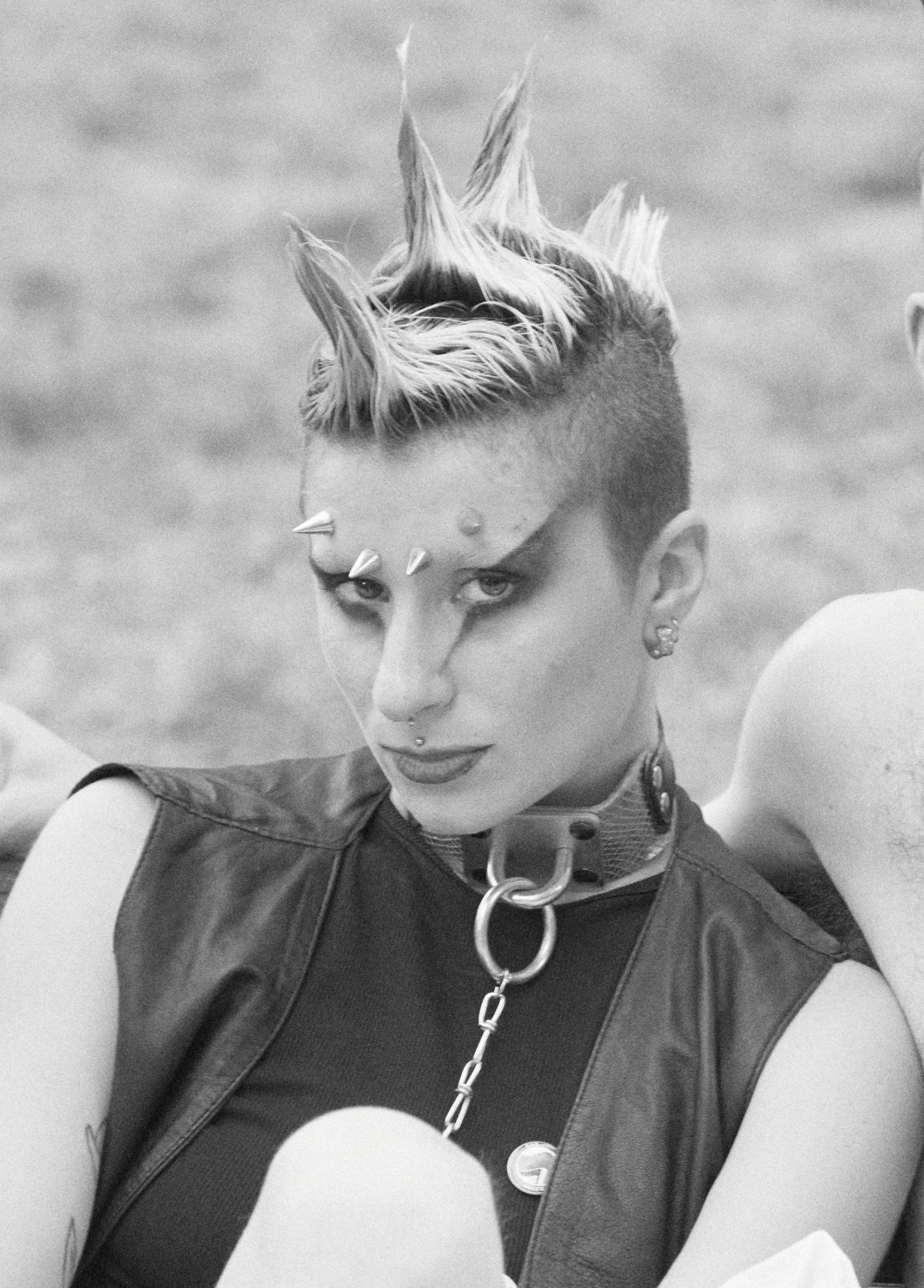 a black-and-white portrait of a punk with facial piercings, studs, and 70s eye make-up. they are wearing a leather waistcoat and a collar at milan pride