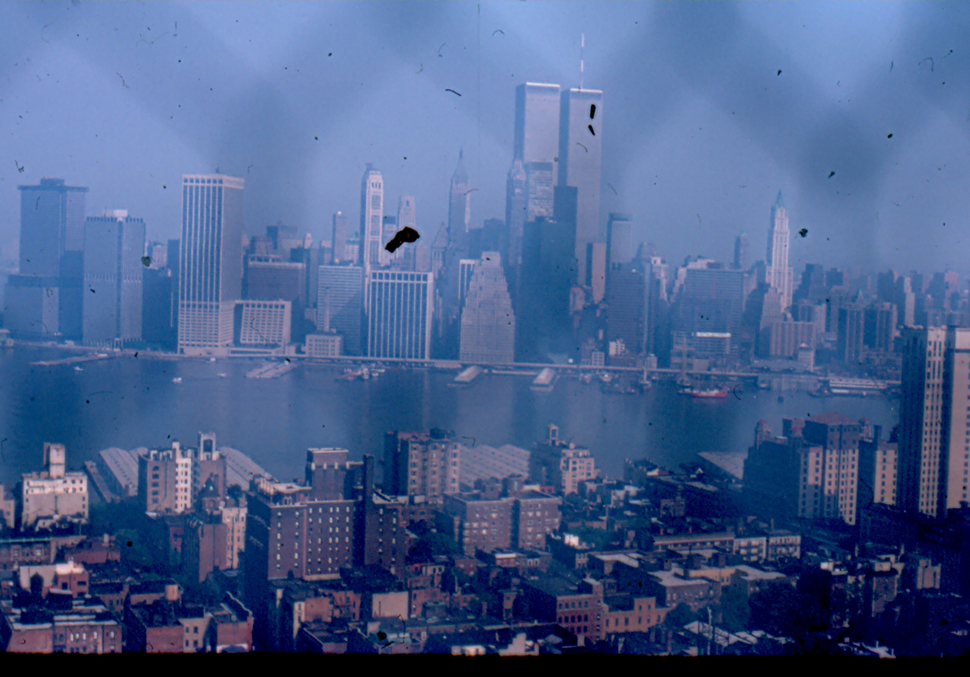 a robert d cave sr. photograph of a new york skyline through a chain fence with the empire state building and the twin towers in the distance.