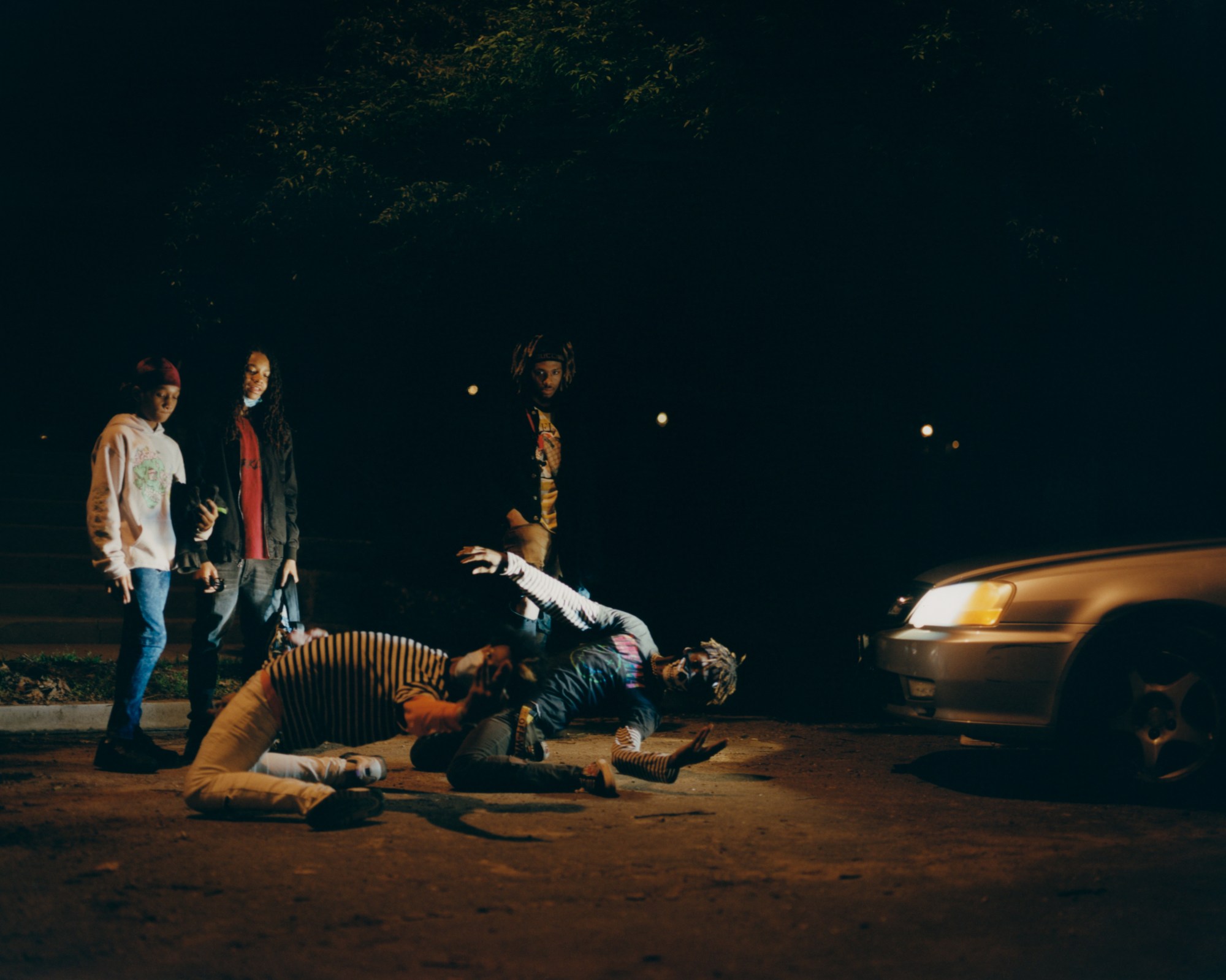 a dance crew photographed in front of car headlights at night