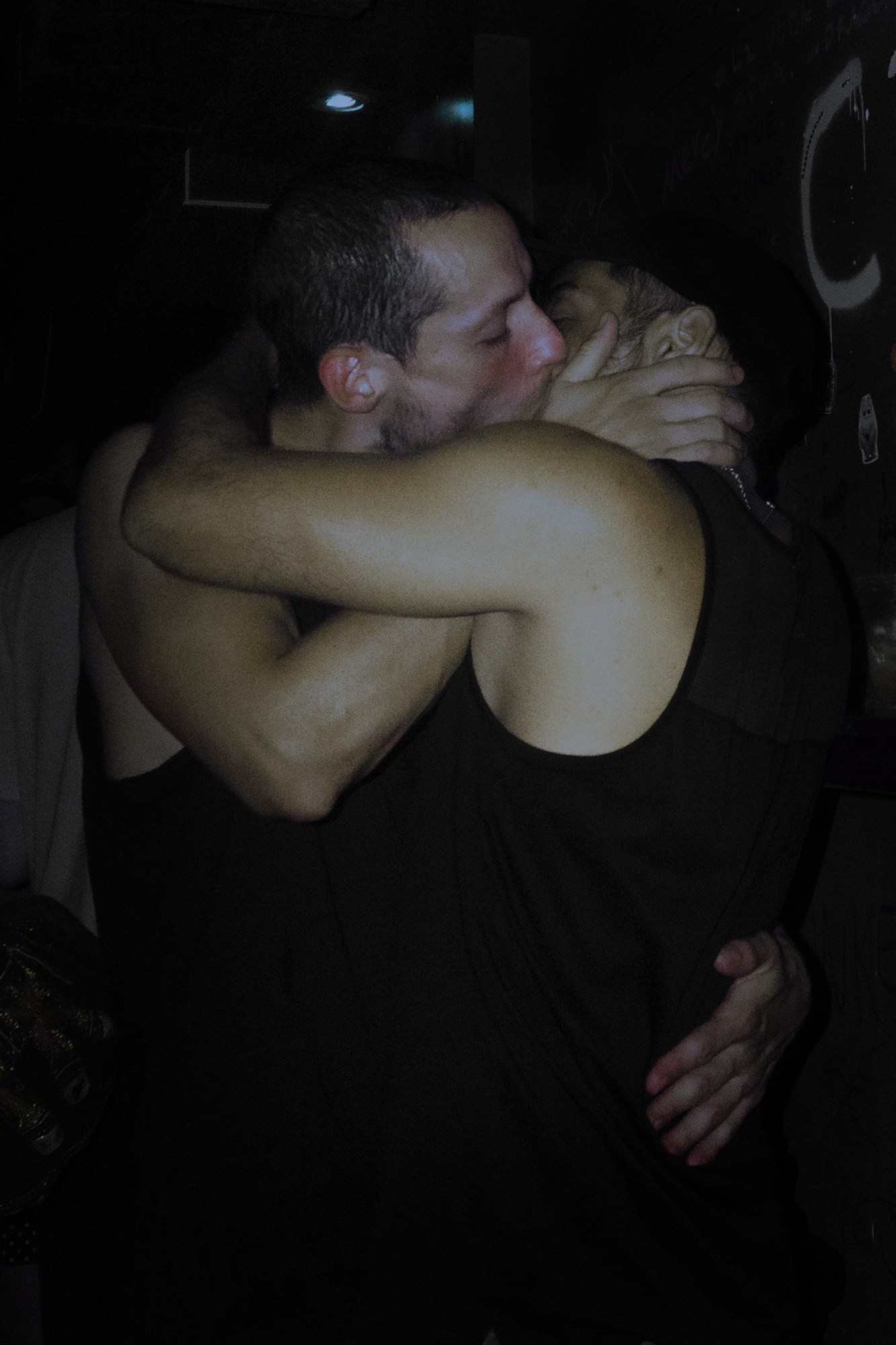 two men in matching black tank tops kissing in a nightclub in argentina