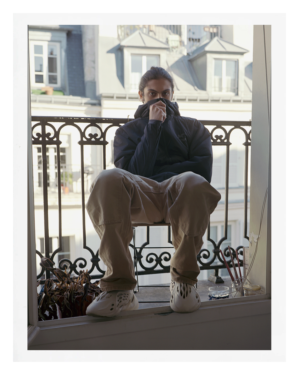 photo of parisian teenager crouching on his balcony covering his face with a hoodie