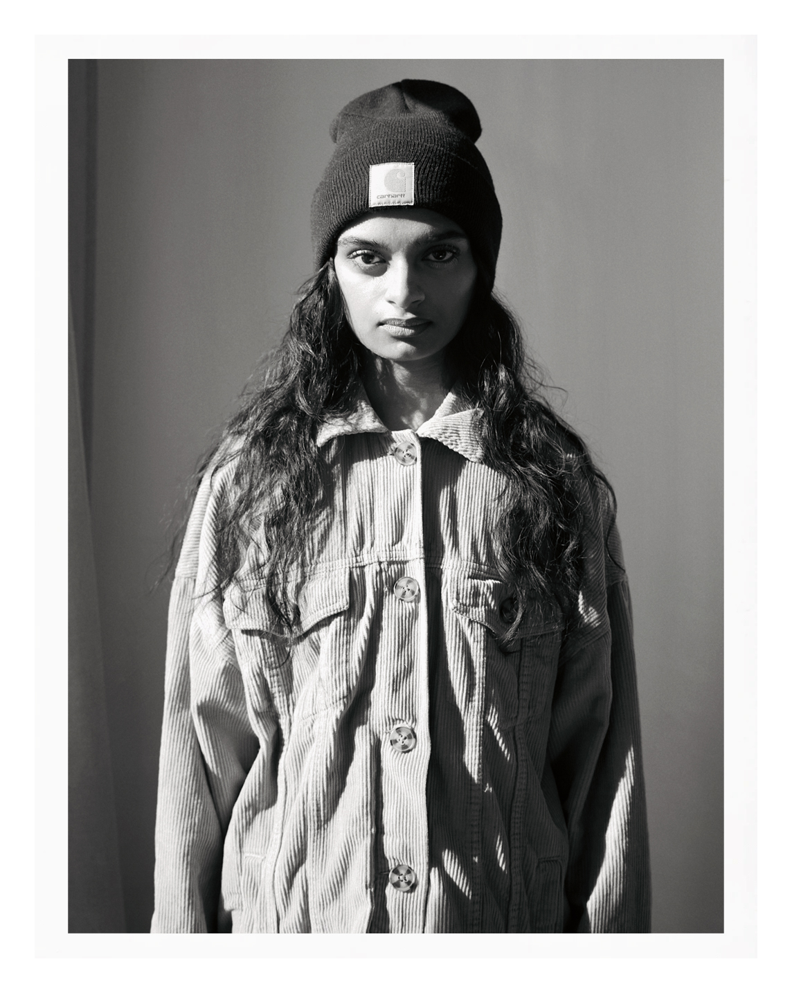 black-and-white photo of parisian teenager standing against a wall in a cord jacket and beanie