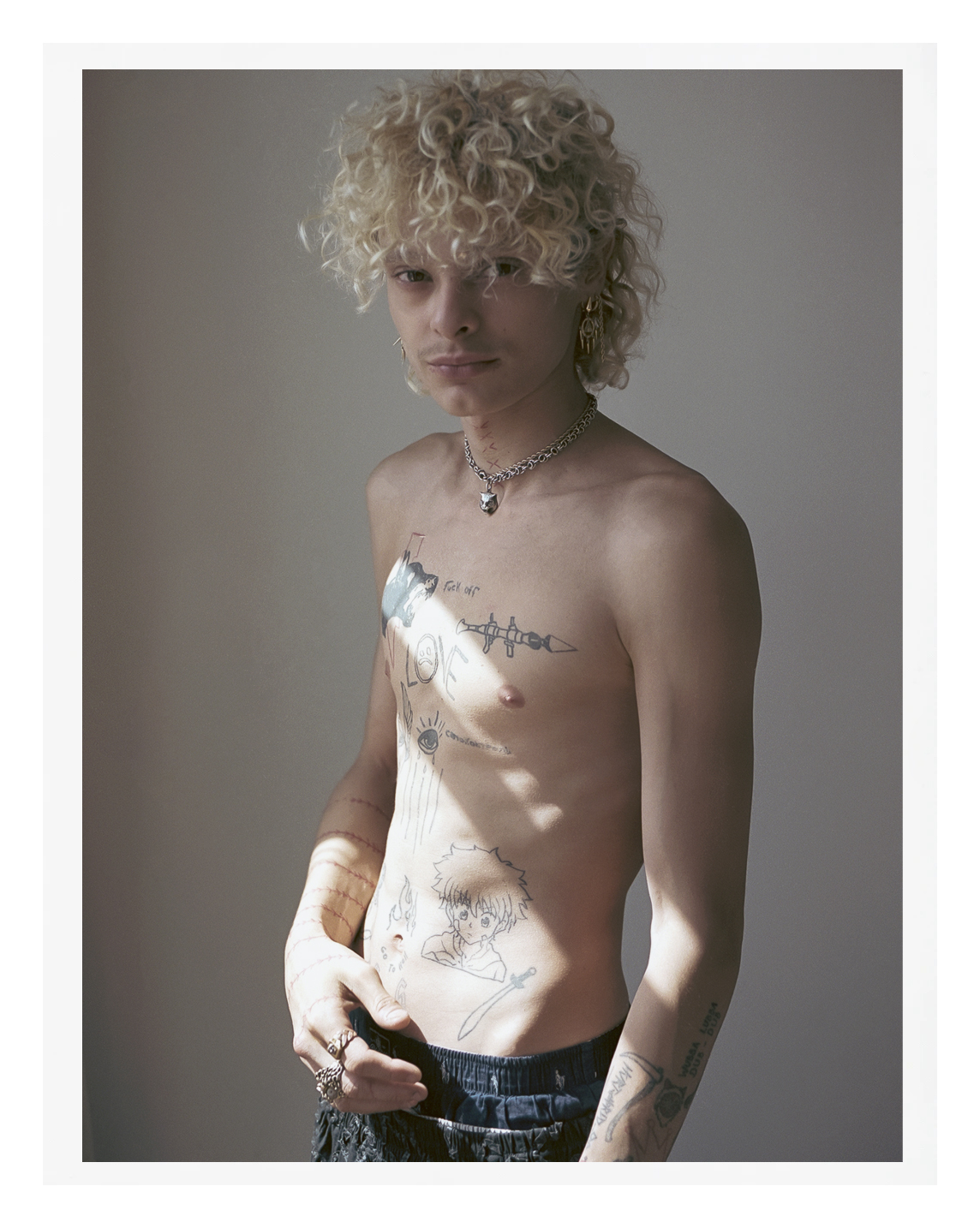 a blonde topless parisian teenager with tattoos standing in sunlight