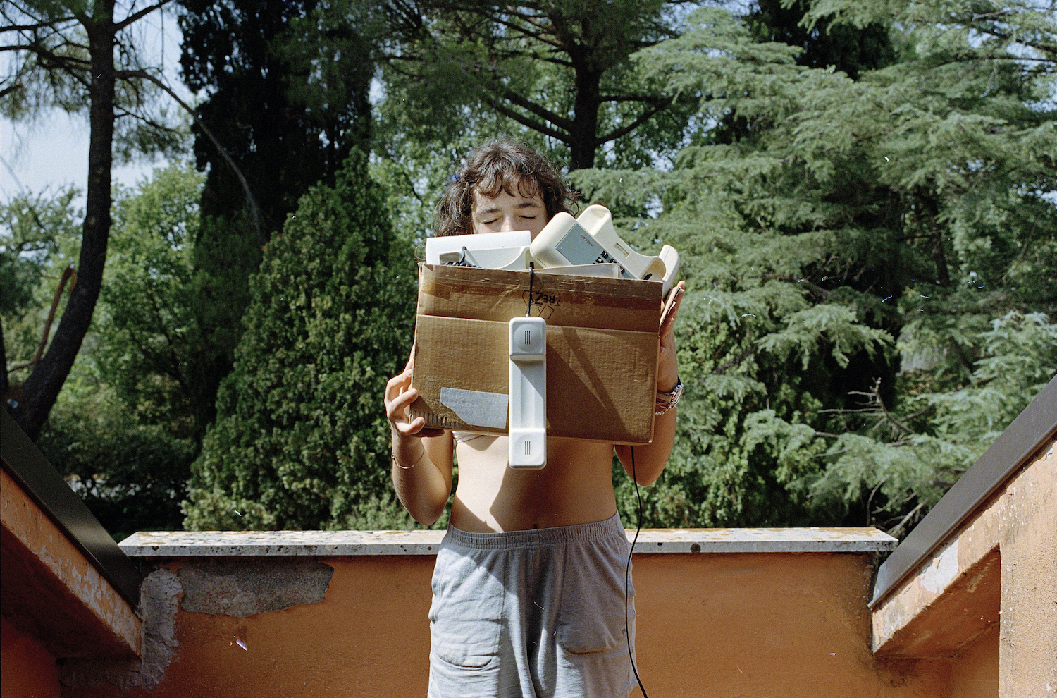 a woman on a balcony holds a cardboard box full of old telephones