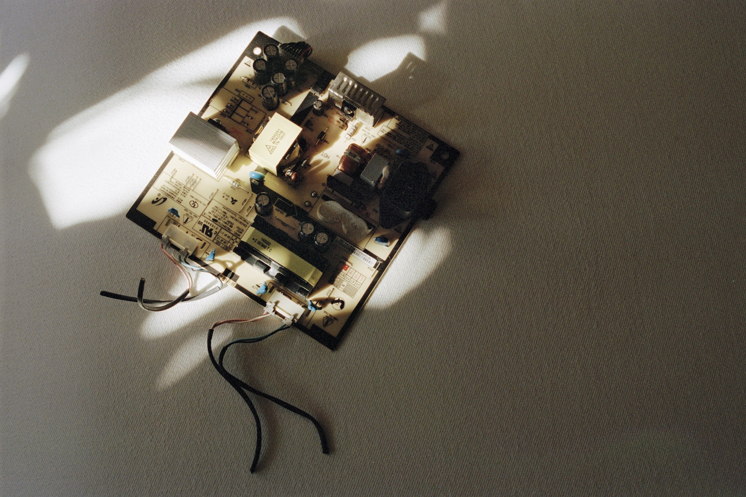 a broken piece of a electronic product against a cream sheet with light and shadow across it