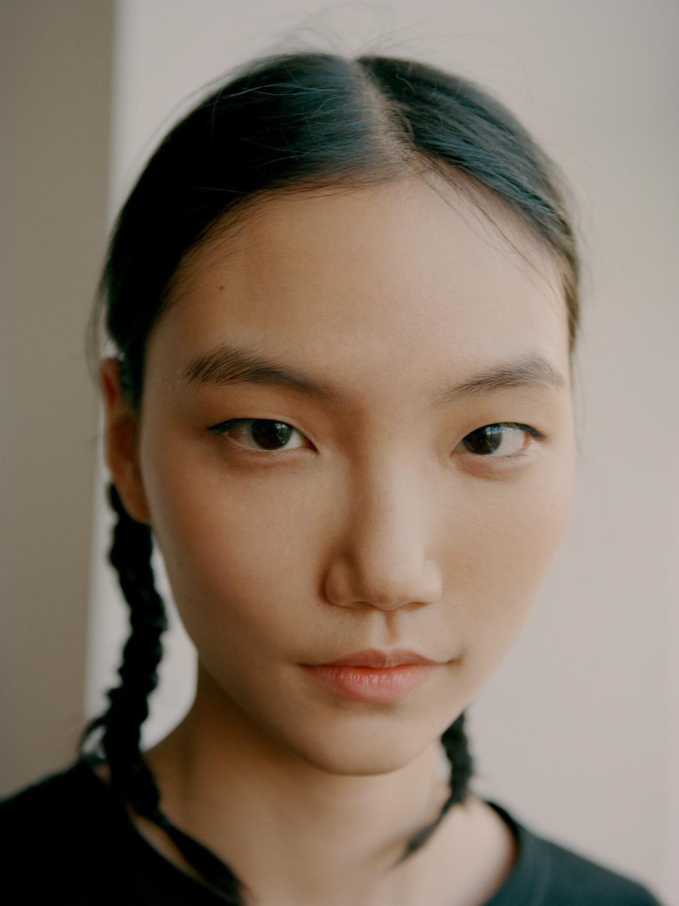 an asian model with her hair in plaits looks to camera with a slight smile