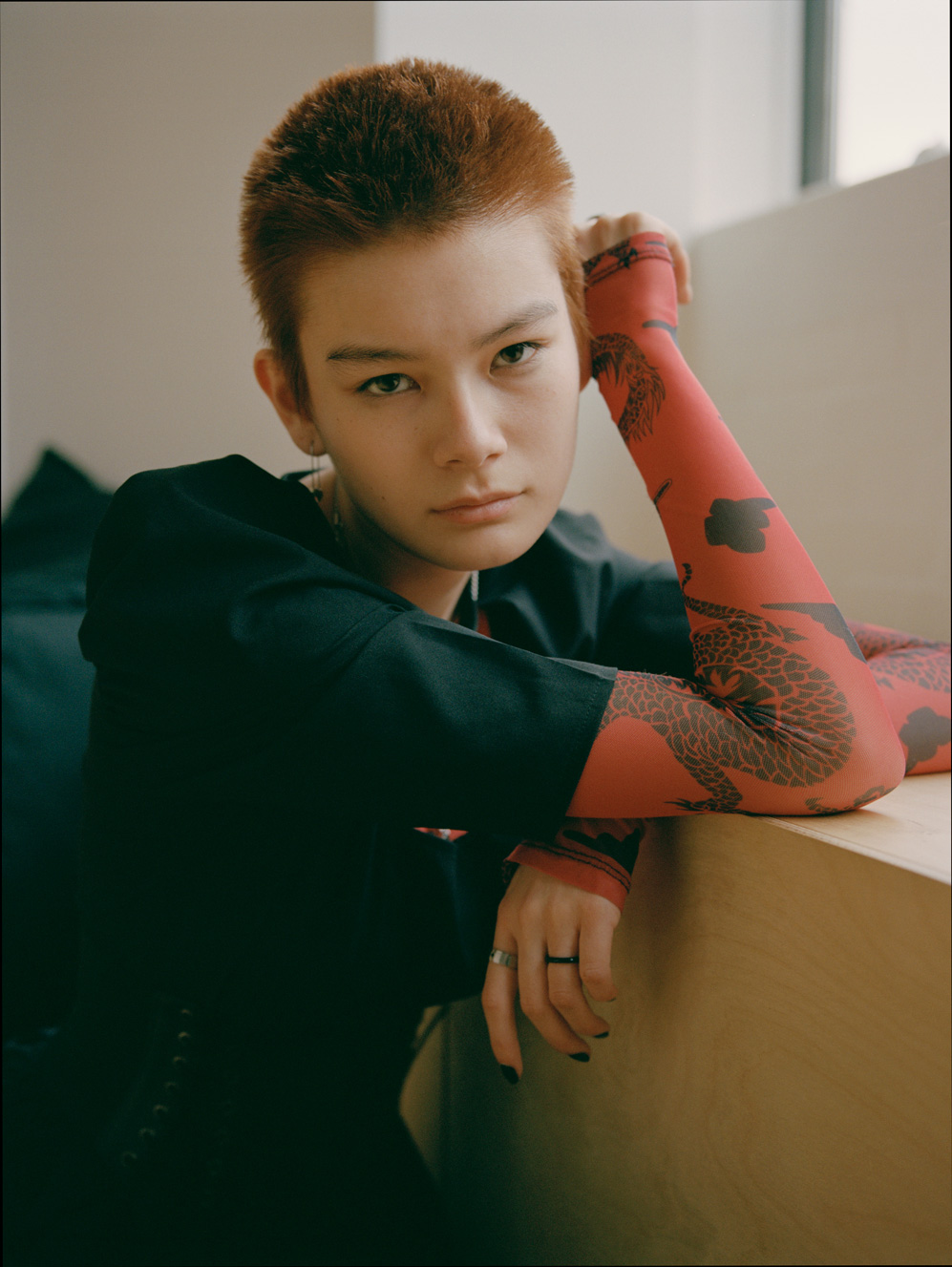 an asian model with cropped dyed hair and dark nail polish leans casually in a window