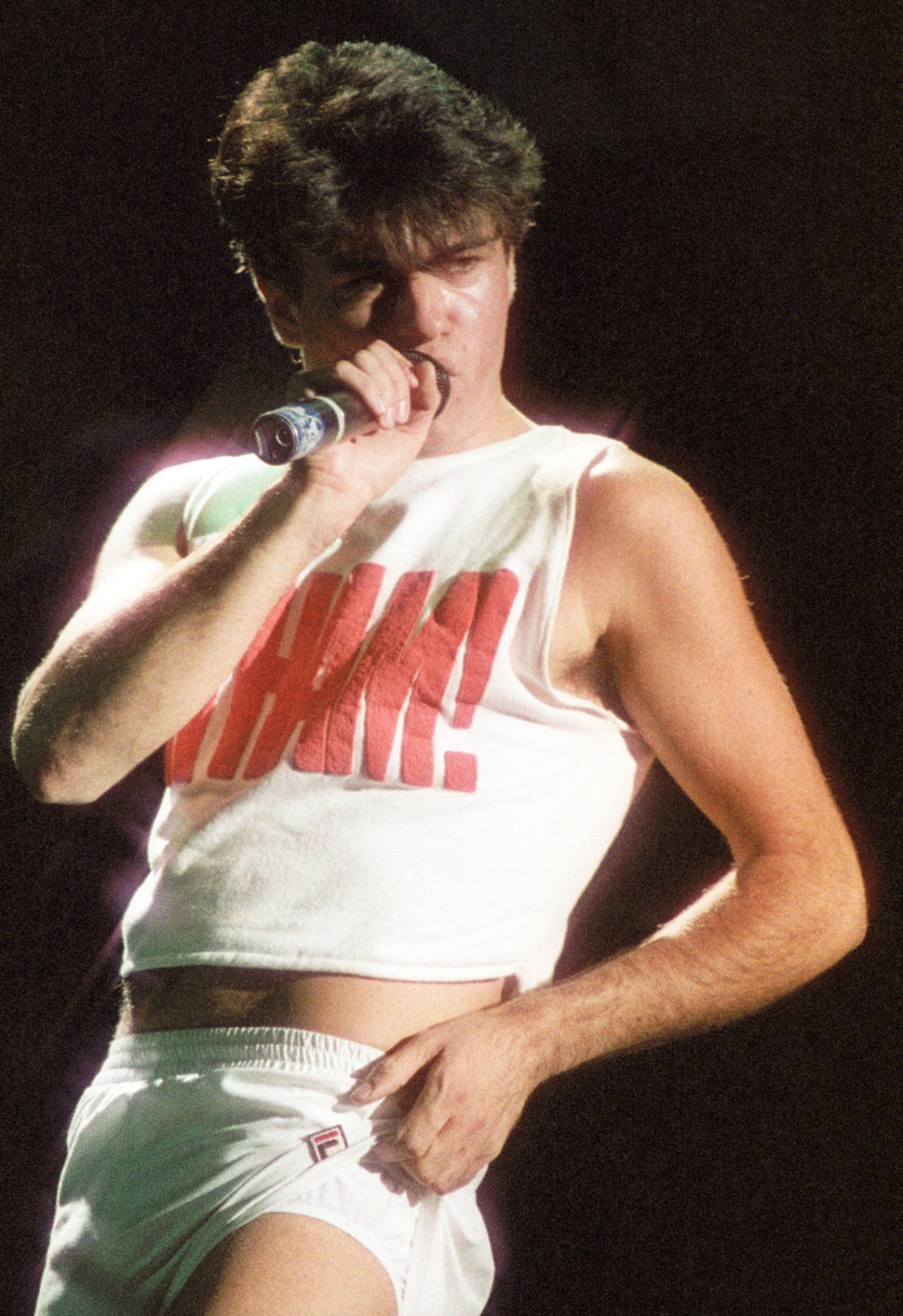 young george michael on stage in white short shorts and a WHAM crop top