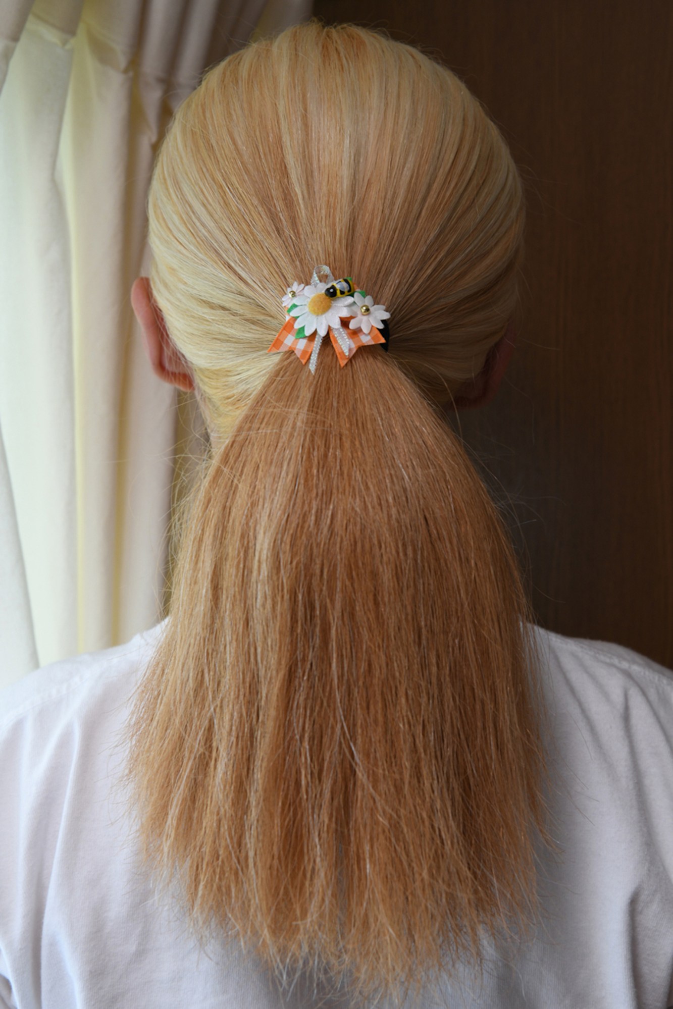 blonde woman's ponytail, shot from behind, held with an orange ribbon