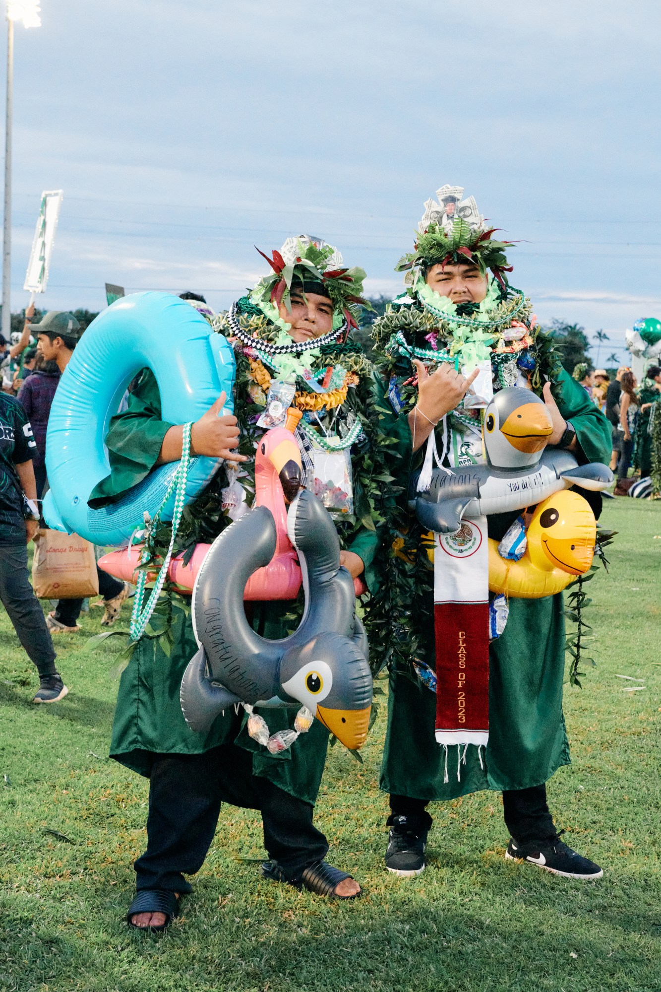 hawaiian students jose and jesus posing in leis and inflatable floats in graduation gowns