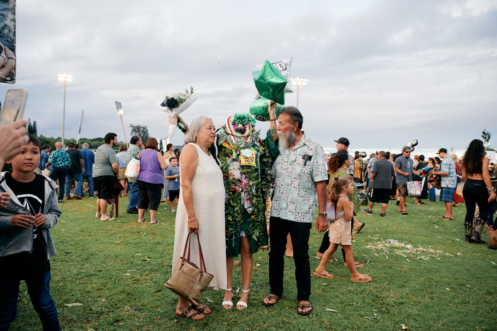 parents and a high school graduate covered in leis and balloons at Kapaʻa High School