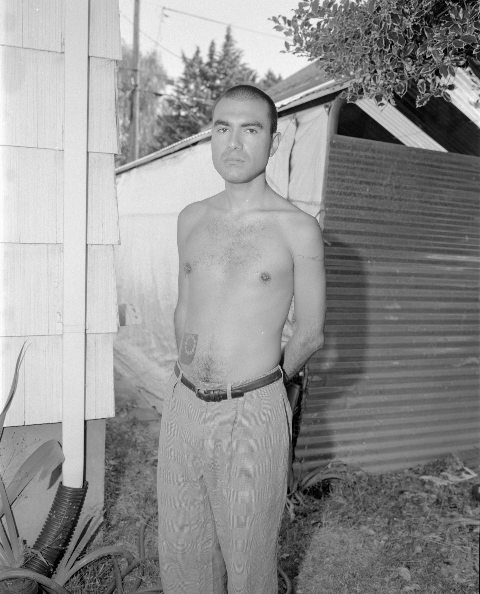 a man with no shirt and slacks posing for a portrait