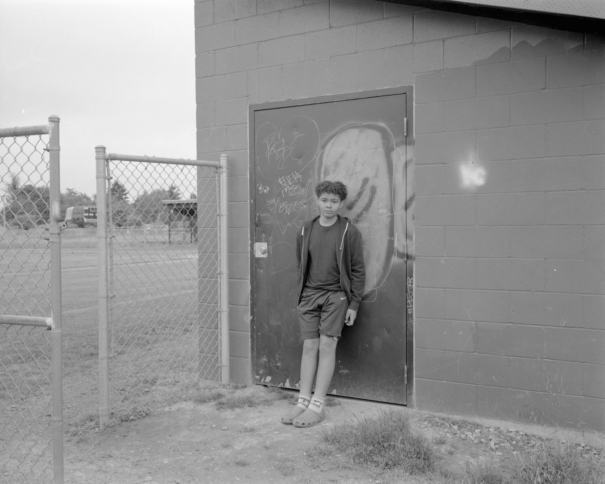 a young man in sports clothes and crocs posing in front of a graffiti covered door