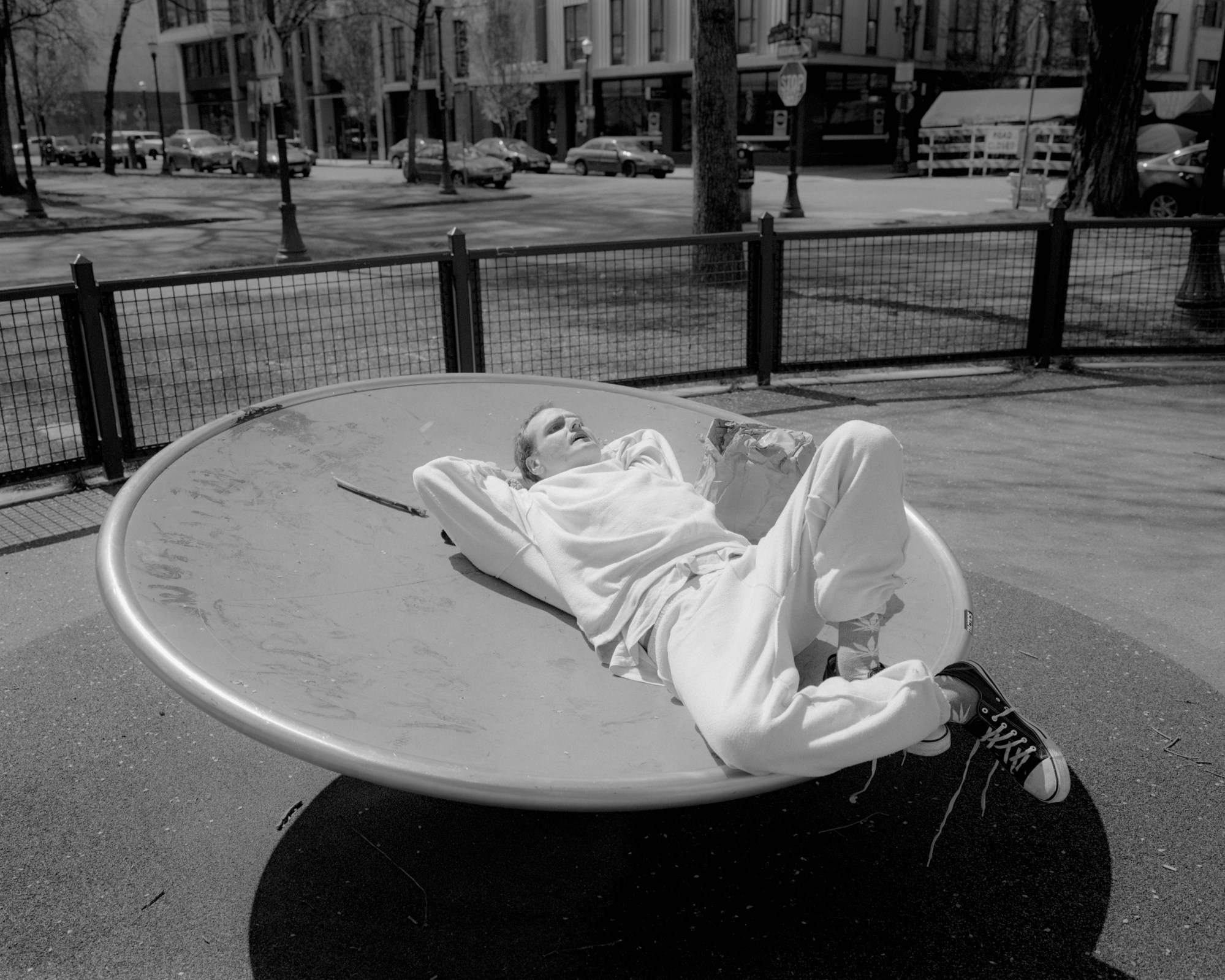 a young person in white sweats and converse lying on a circular surface in a park