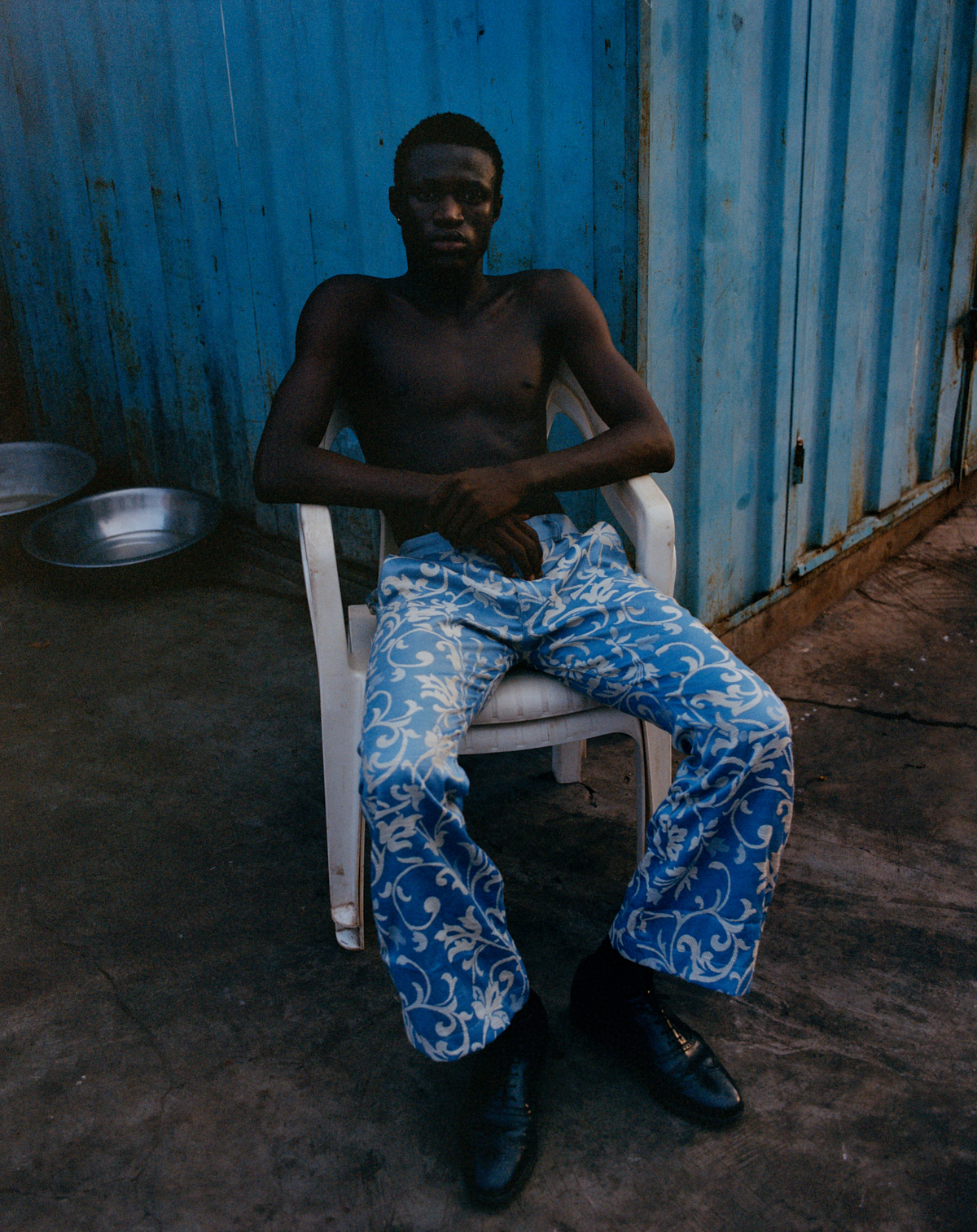 a ghanian boy in blue pants sitting in a chair in front of a blue cargo bin