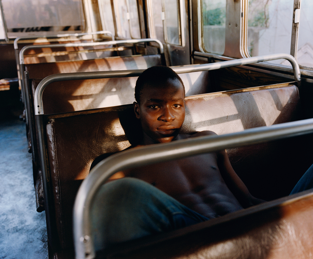 a young boy sitting in a row of brown bus seats photographed by kyle weeks