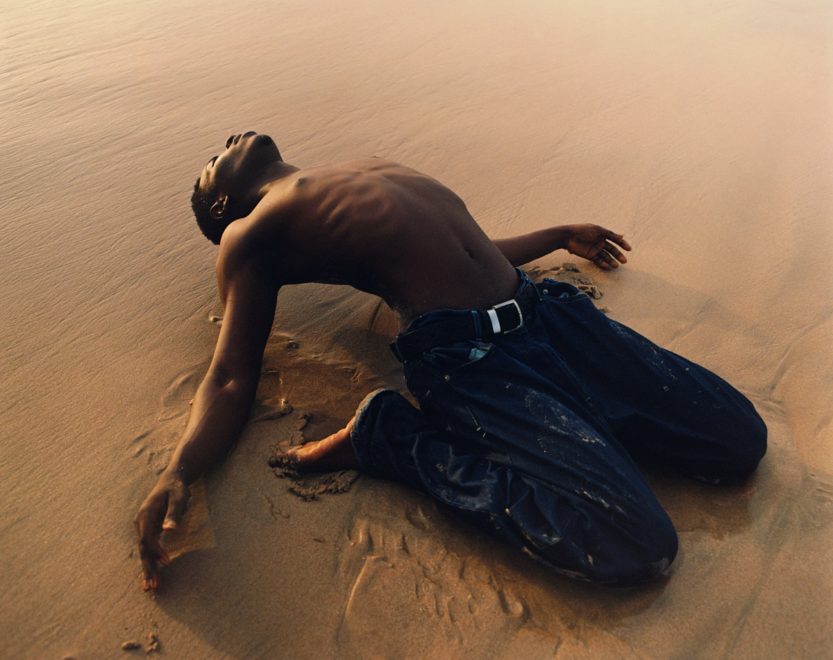 a boy with his shirt off arching his back in the sand in ghana