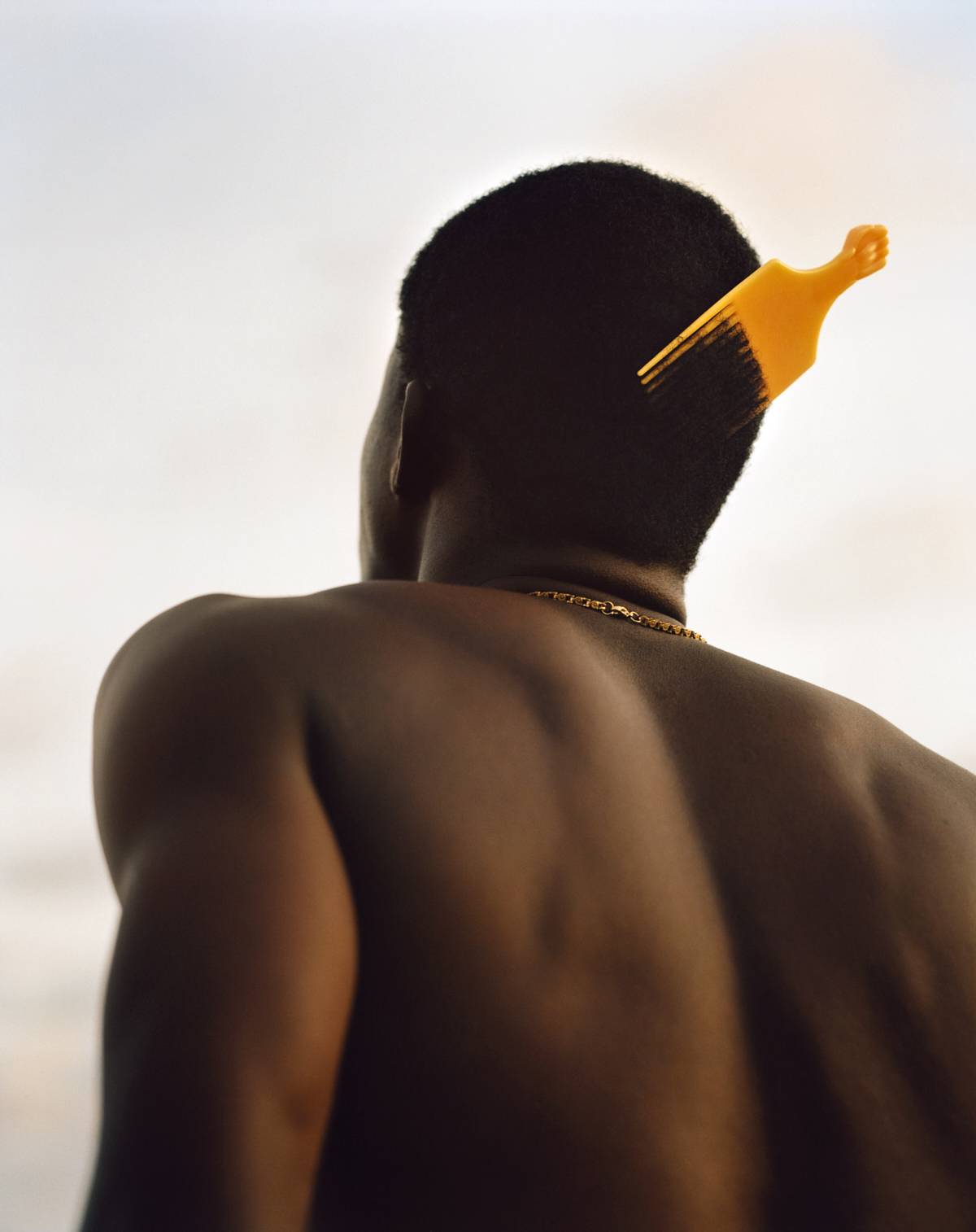 the back of a man's head with a yellow hair pick photographed by kyle weeks in ghana