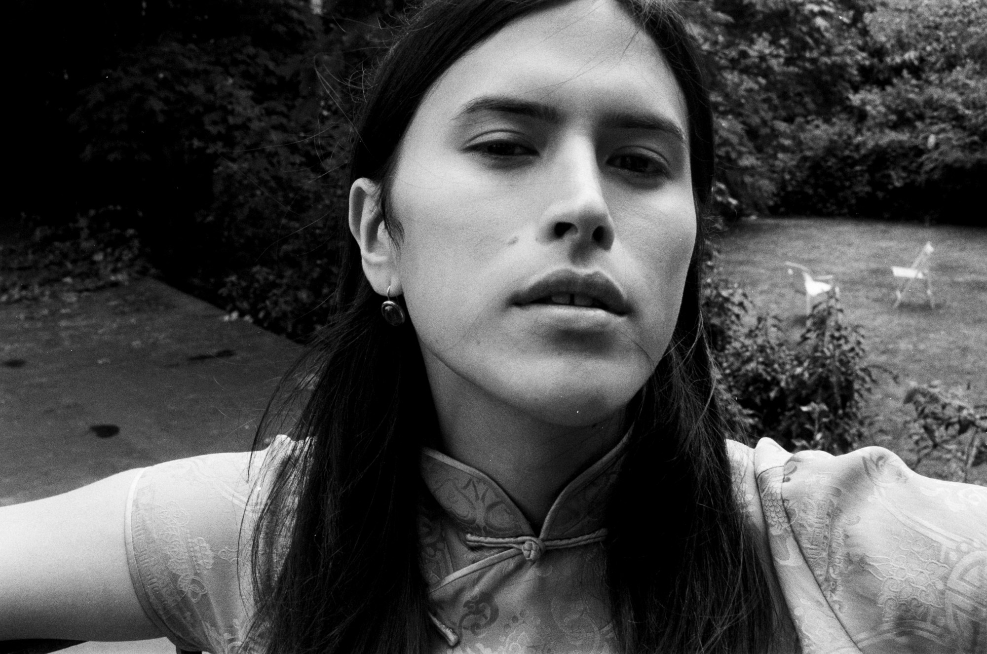 a black and white portrait of bellies author nicola dinan in a garden. she wears a silk dress. she is looking into the camera.