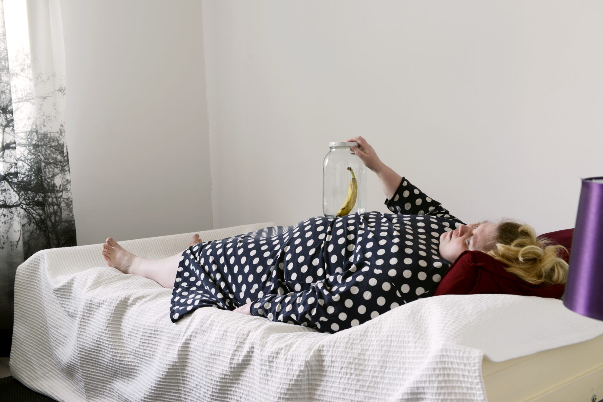 a woman lying on a bed in a polka dot dress holding a banana in a glass jar