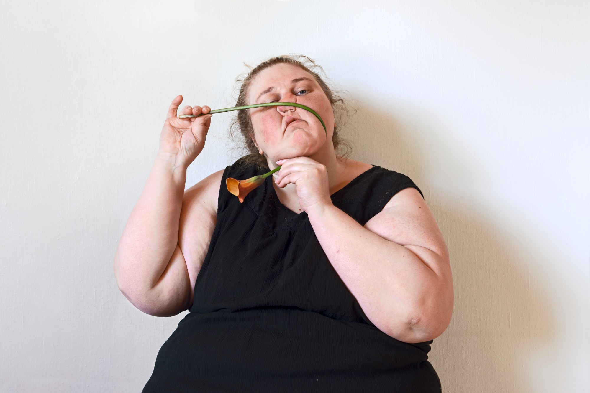 a woman stretching an orange flower over her squished face