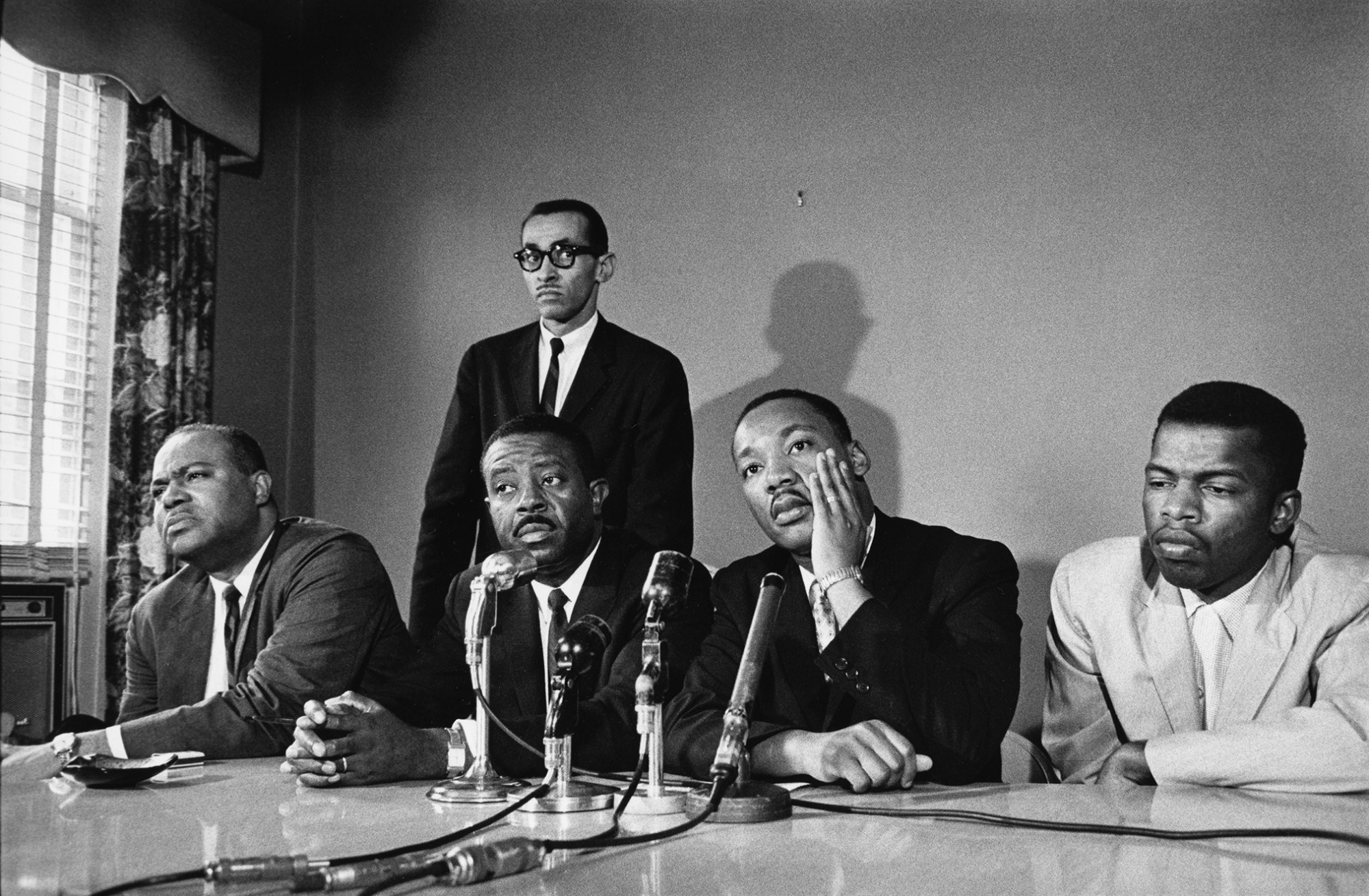 John Lewis, Martin Luther King Jr., Ralph Abernathy, and James Farmer sit in front of a table of microphones at a press conference