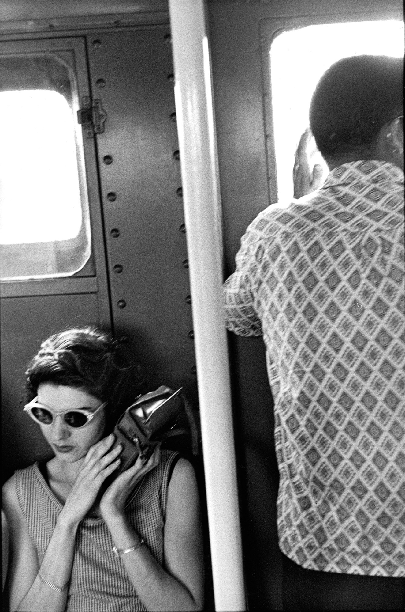 a white woman in cat-eye sunglasses sits on the subway resting her head on her handback