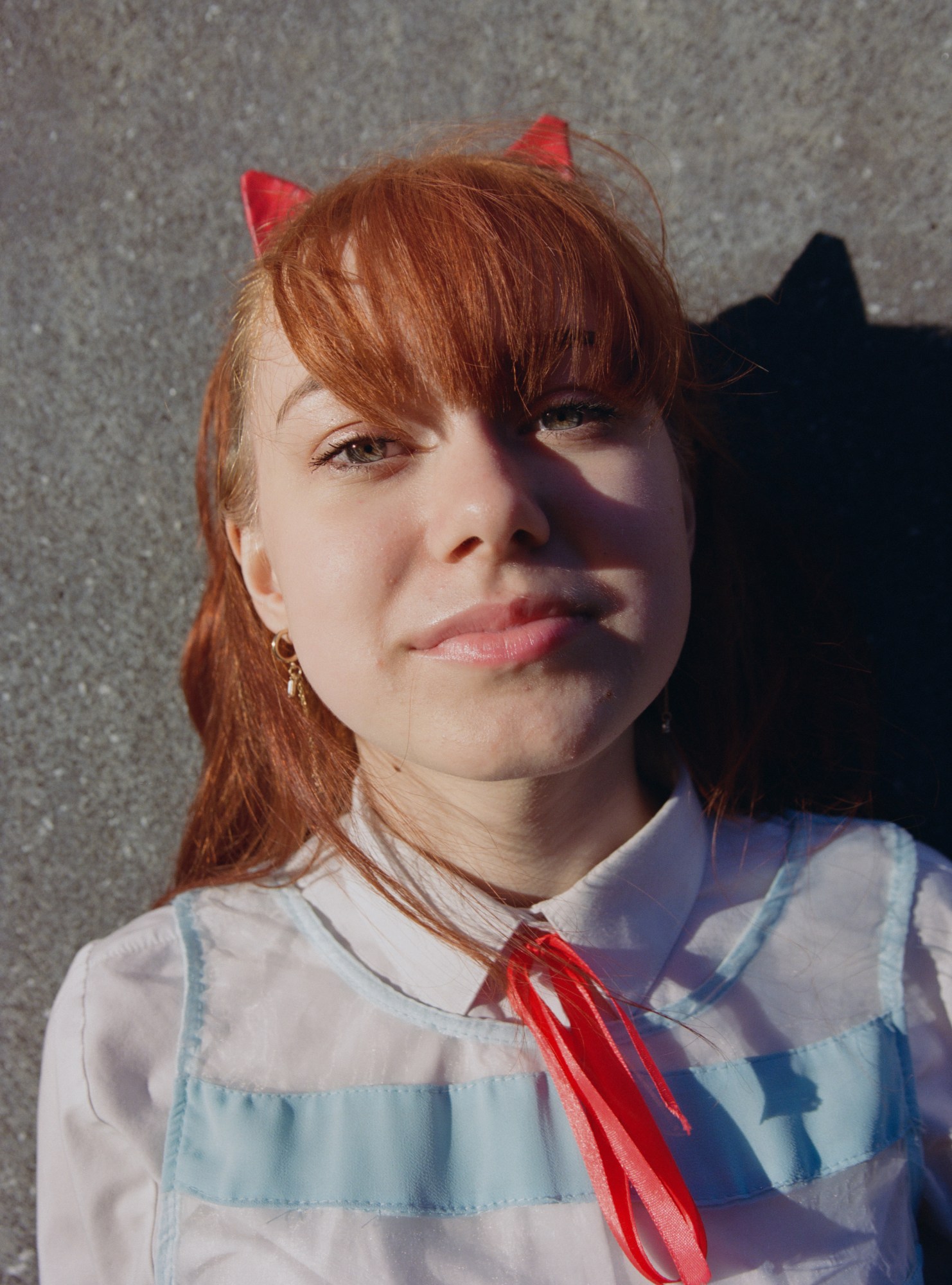 a person with long red hair wears a white shirt with a red ribbon tied around the neck