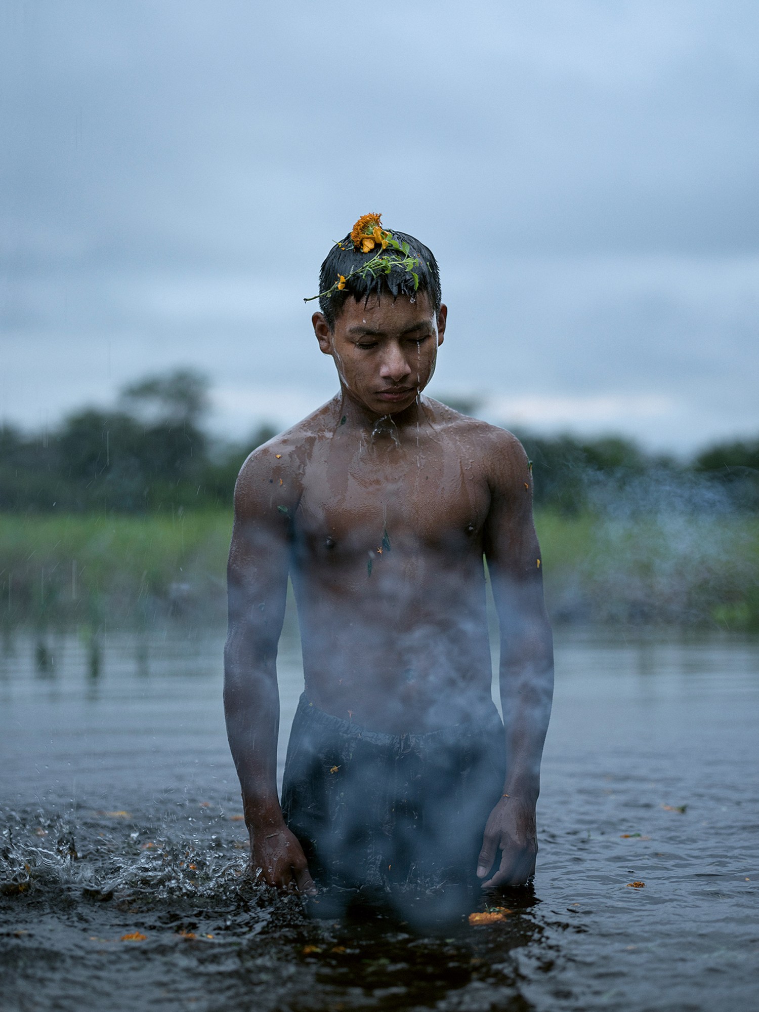 a young man photographed bathing in a river in the amazon; he has a few orange flowers on his head