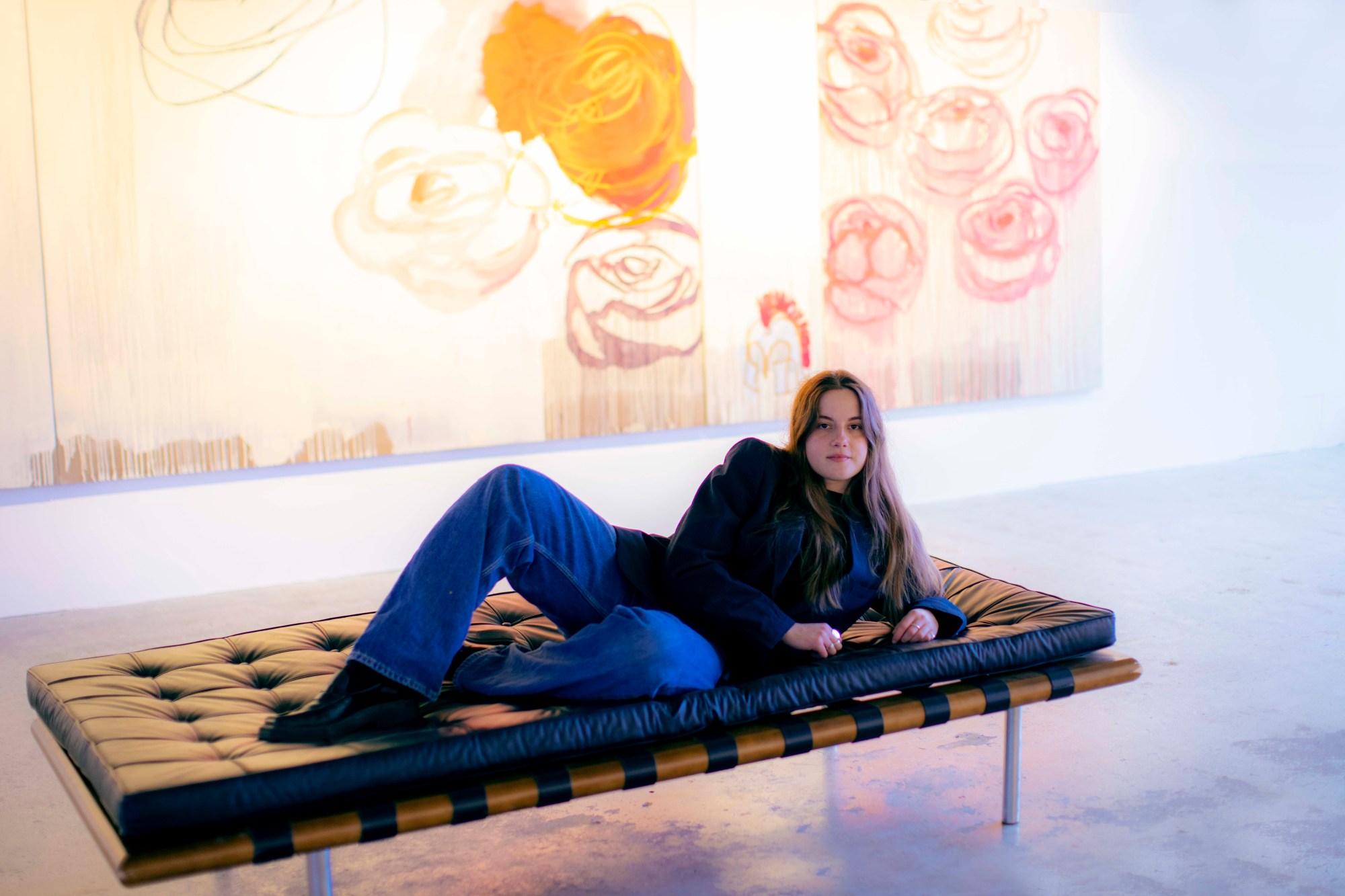 ellie pennick lying on a lounge chair in front of artwork in guts gallery